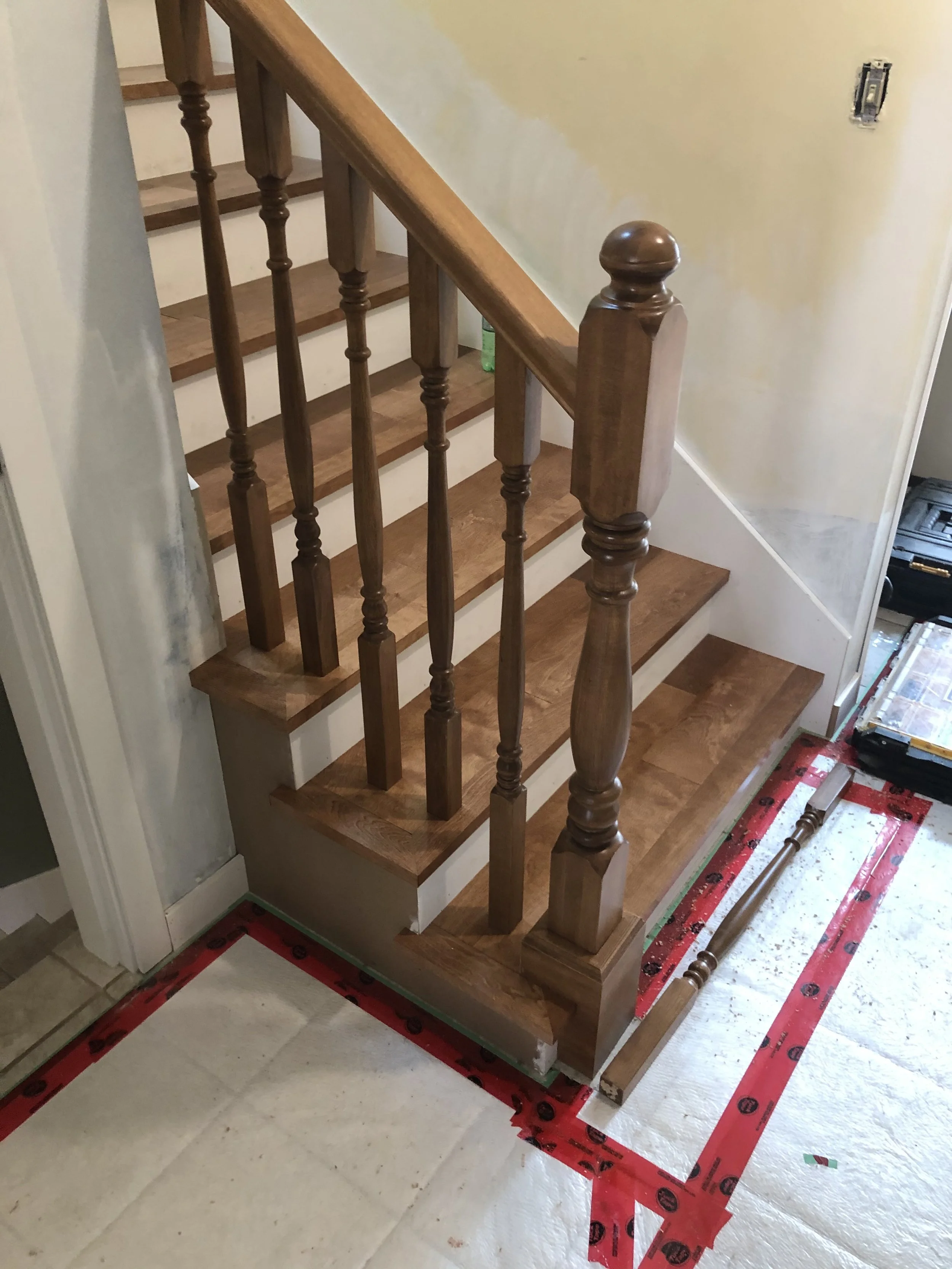 Wooden staircase with railing in the process of installation, protective red tape and tools on the floor.