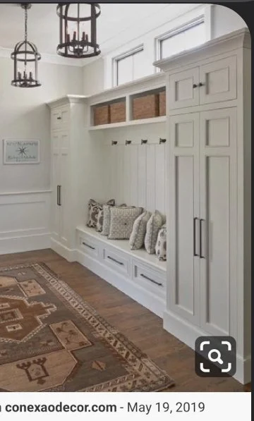 White built-in storage with a bench, pillows, hooks, and cabinets in a room with hardwood floors and a rug.