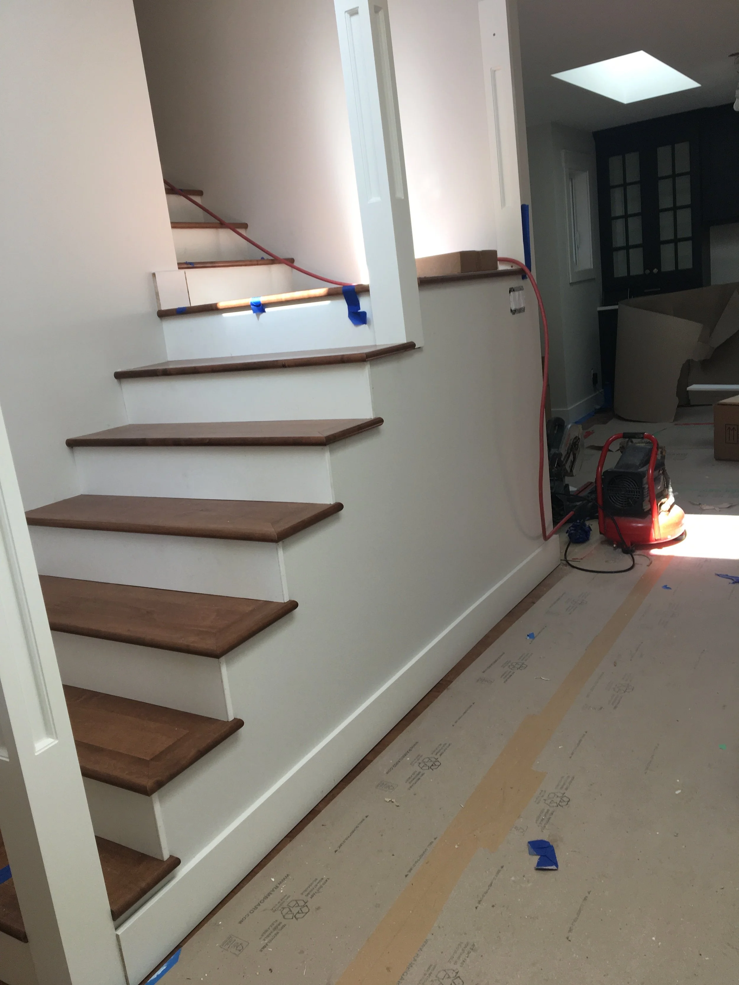 Interior view of a house under construction, showing stairs with wooden treads, some construction tools, and materials on the floor.