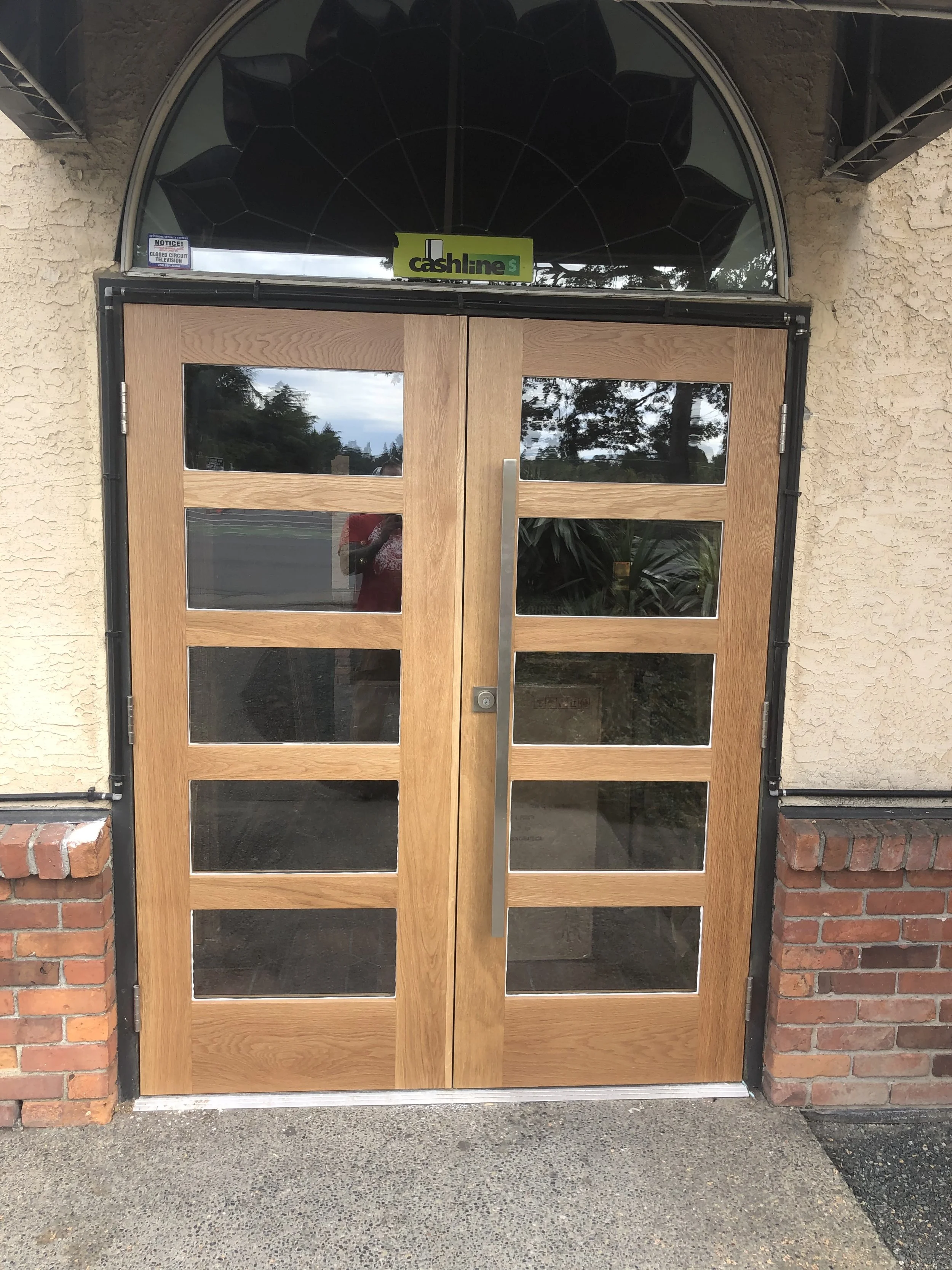 Wooden double doors with glass panels, set in a brick and stucco wall, with a metal handle on the right door.