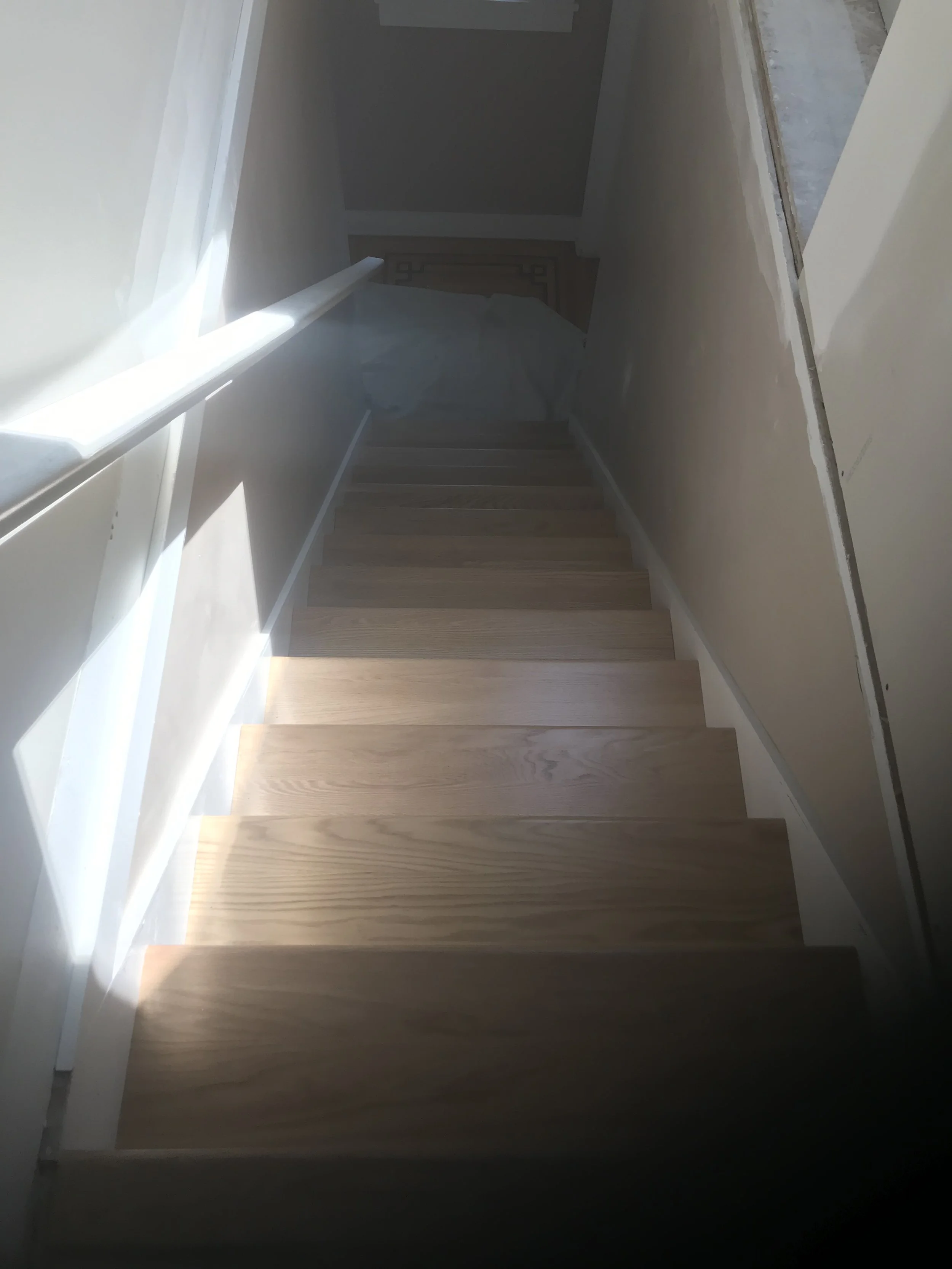 An indoor staircase with wooden steps and white walls, viewed from the top looking down.