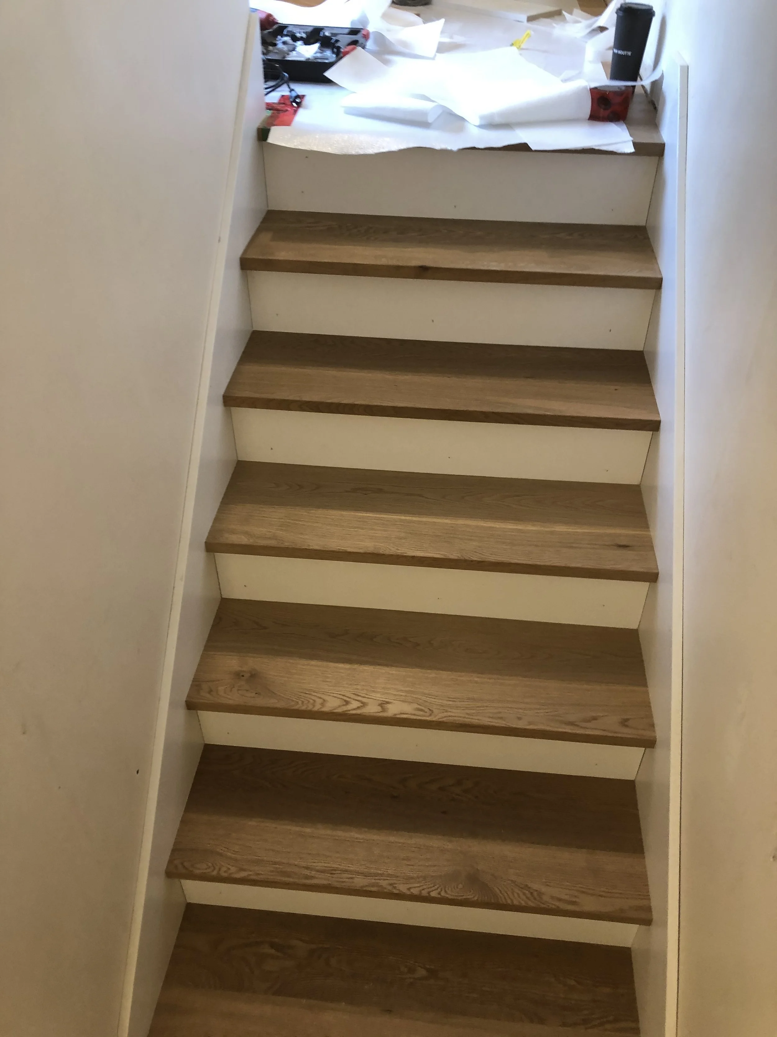 A staircase with wooden steps and white sides, leading upwards, with construction or renovation materials scattered at the top.