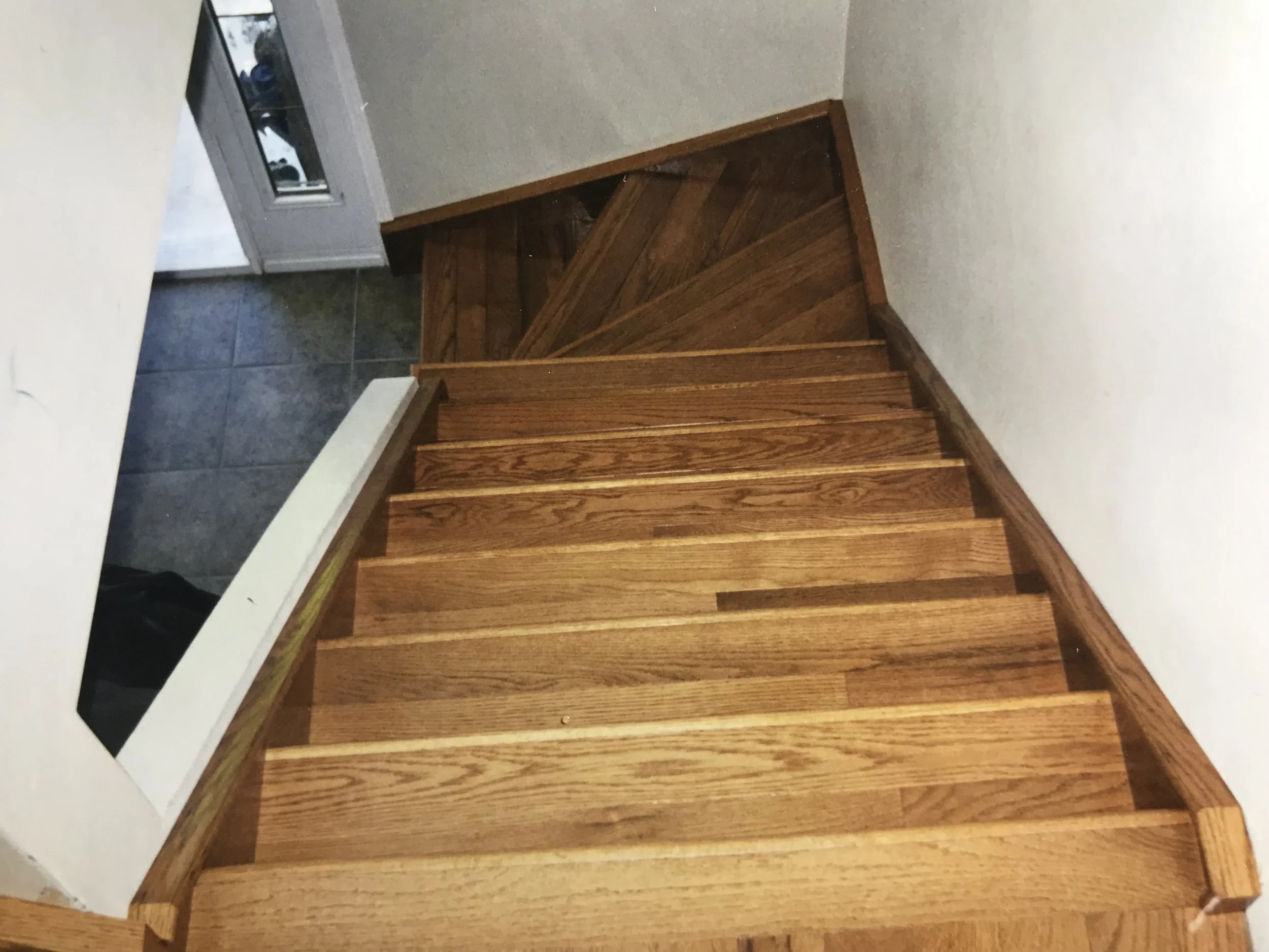 Wooden staircase leading up to a doorway with a glass window, with a hardwood floor and white walls.