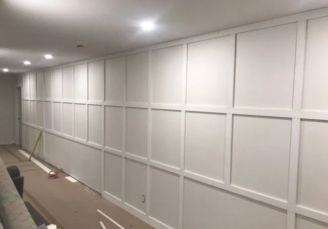 Interior view of a room with a large white paneled wall, recessed lighting, and some construction materials and tools on the floor.
