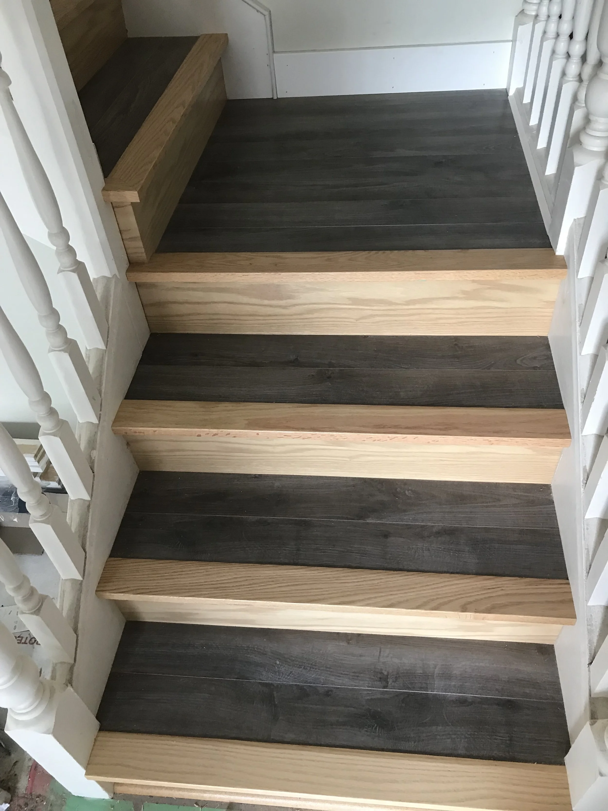 Staircase with wooden steps, dark and light wood alternating each step, white railing on the side.