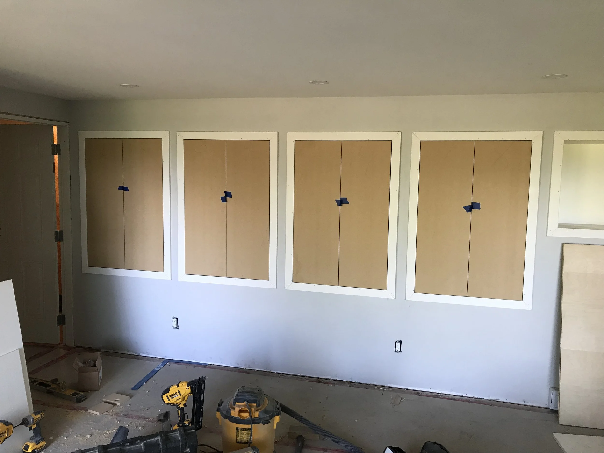 Unfinished interior room with wall panels, construction tools, and electrical outlets, indicating ongoing renovation or construction work.