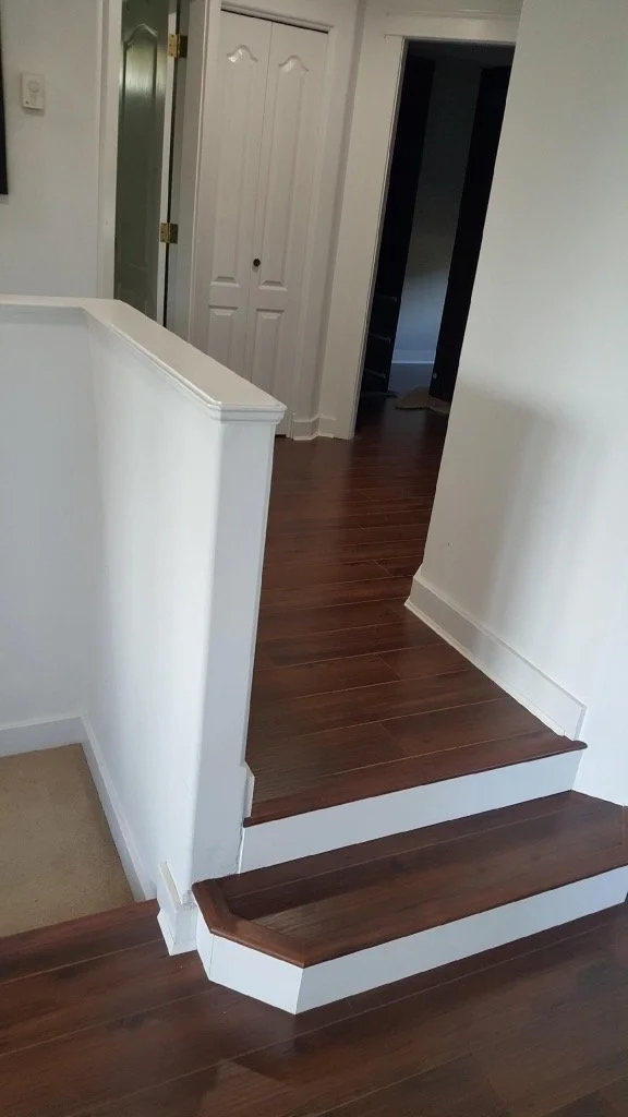 Interior view of a house with wooden flooring, a small step with two steps leading upstairs, white walls, closet doors, and a doorway to another room