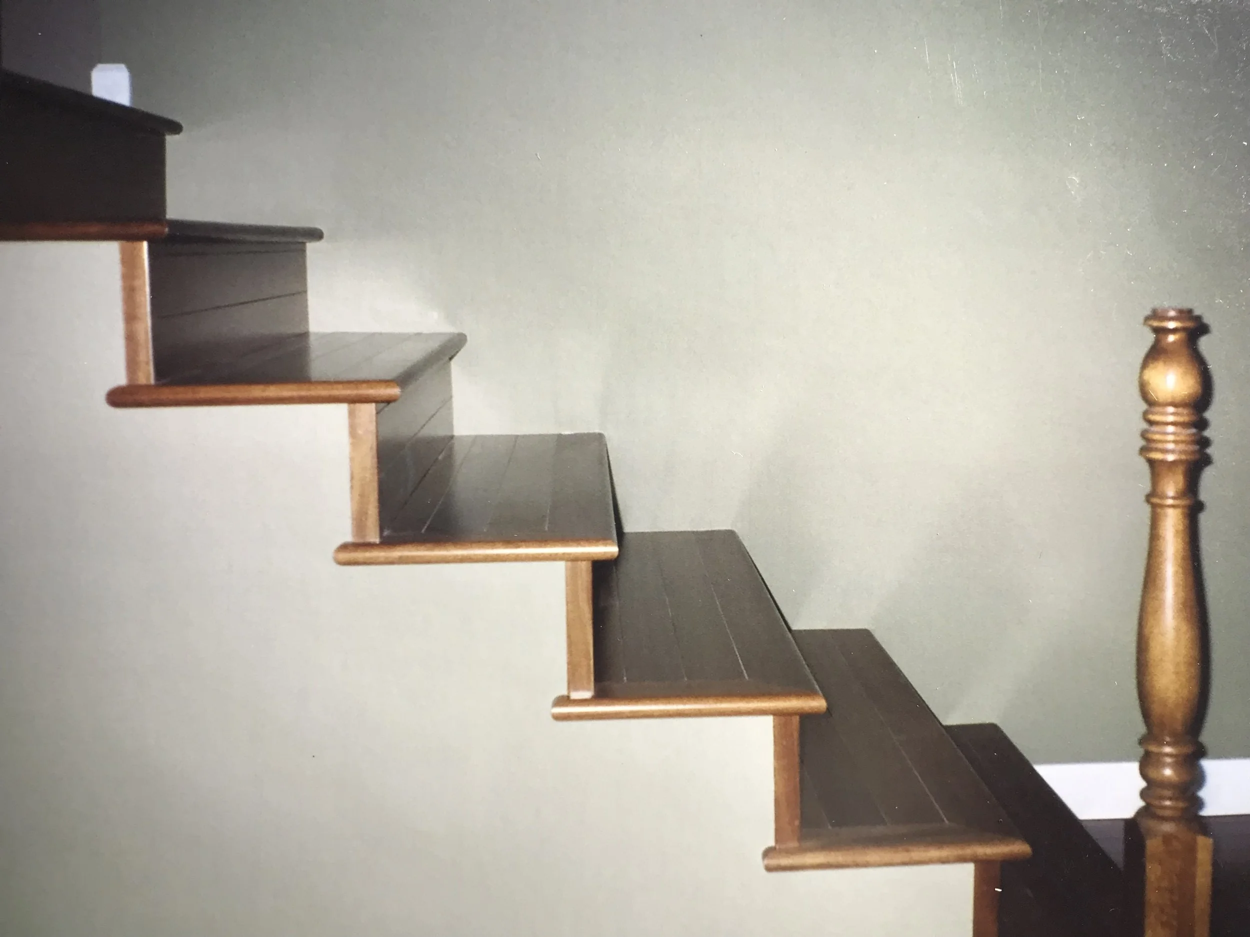 A staircase with wooden steps and banister, leading up beside a plain green wall.