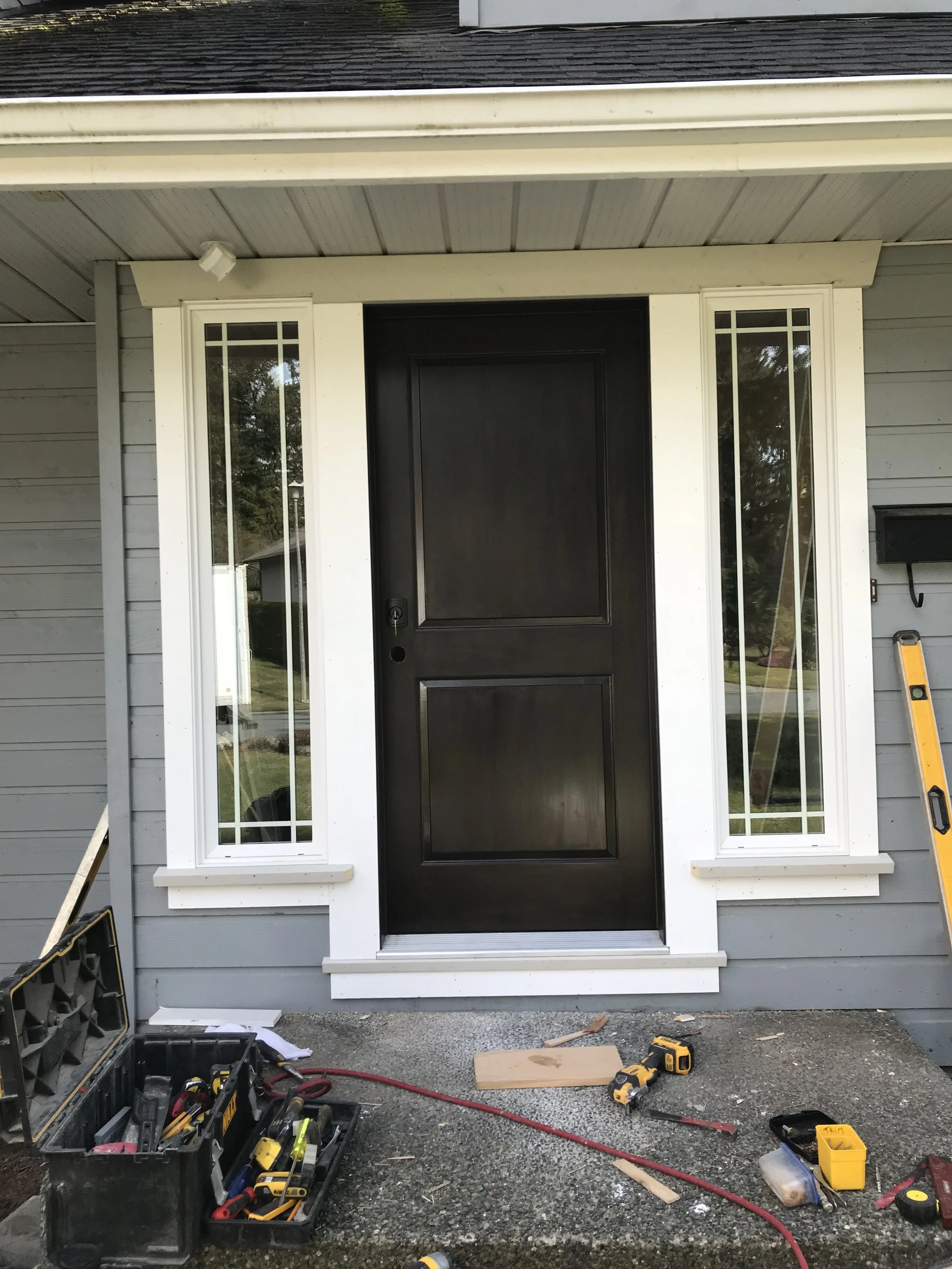 Front door of a house under construction with tools and equipment on the ground, including a toolbox, cordless drill, level, and extension cord.