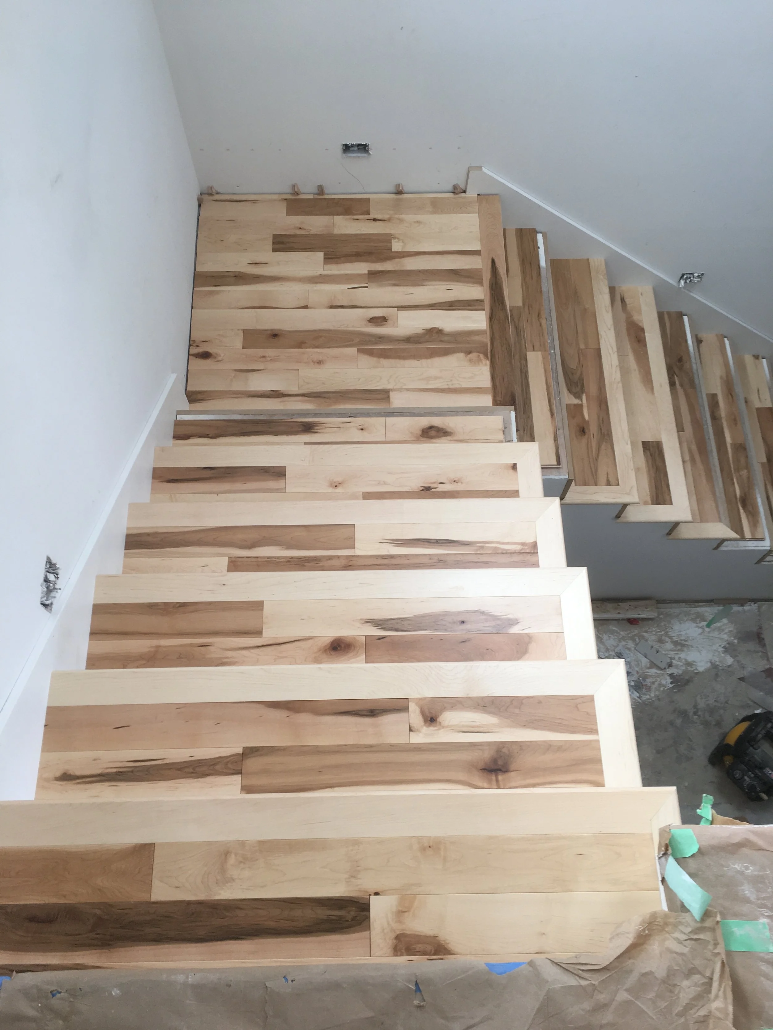Wooden stairs being constructed with unfinished wooden planks, partially covered with painter's tape, in a room under renovation.