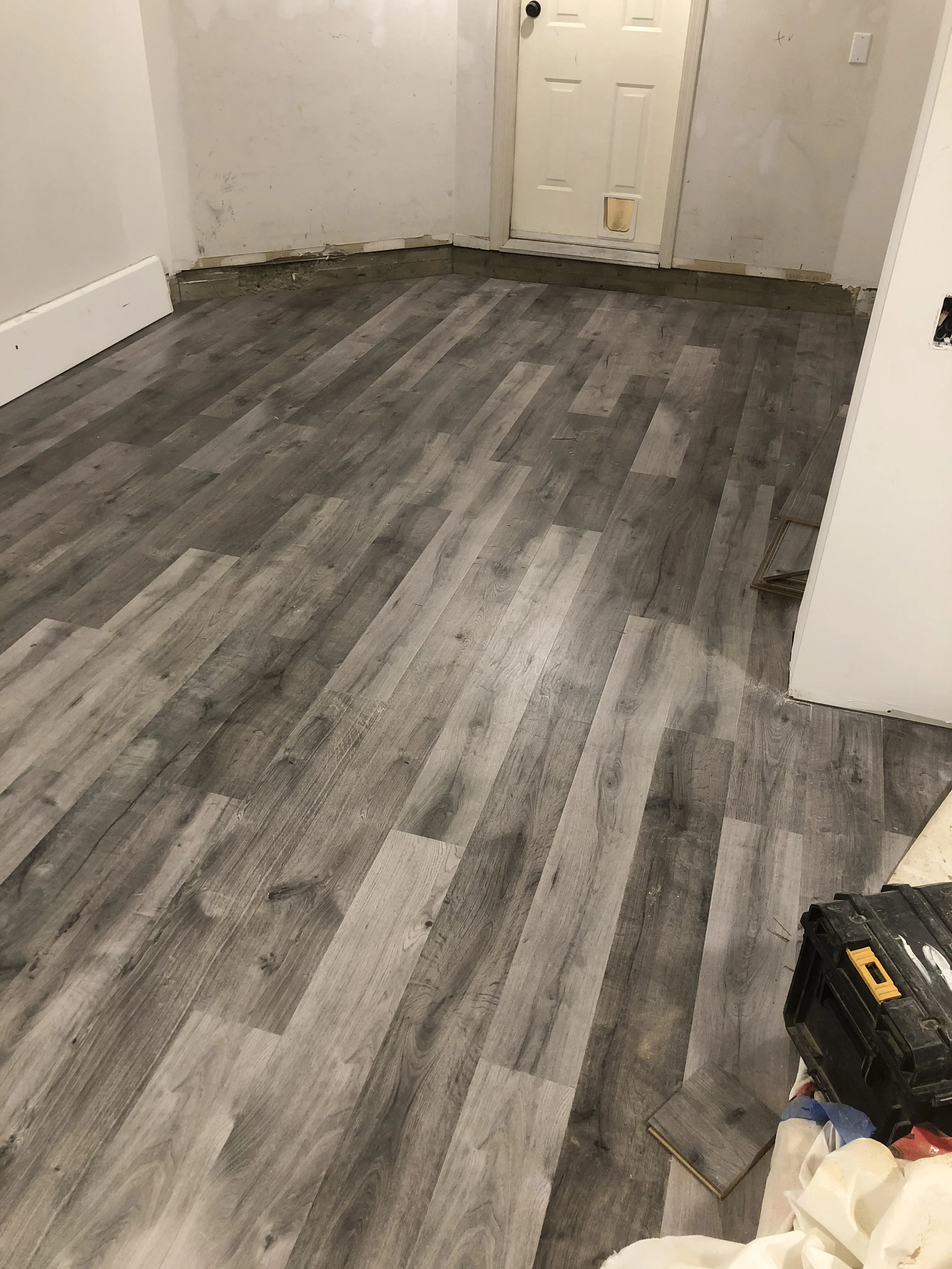 A room with newly installed gray wood-look flooring, partly finished walls, and construction tools and supplies on the floor.