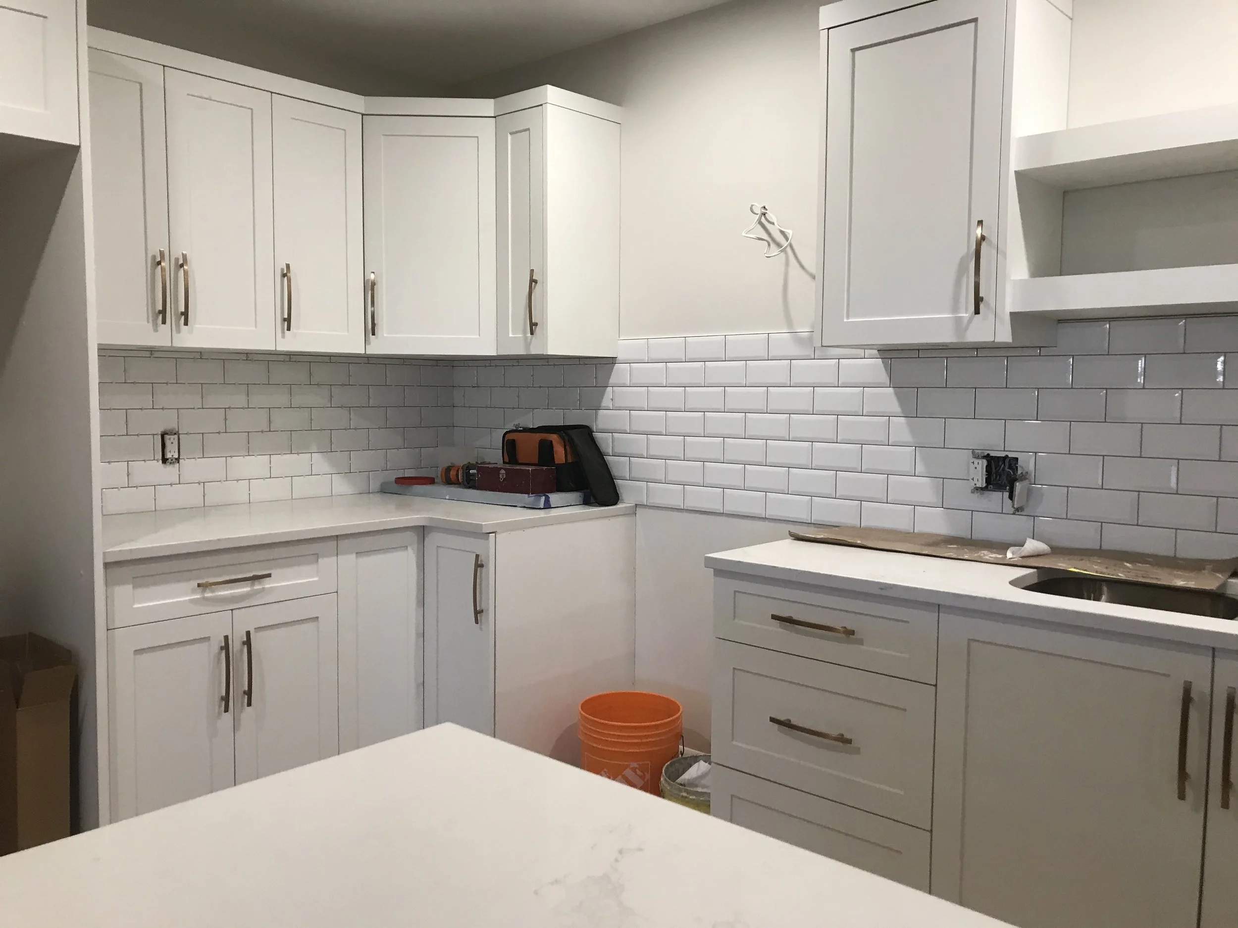 Kitchen with white cabinetry, gray handles, and a white subway tile backsplash, with tools and supplies on the counter.