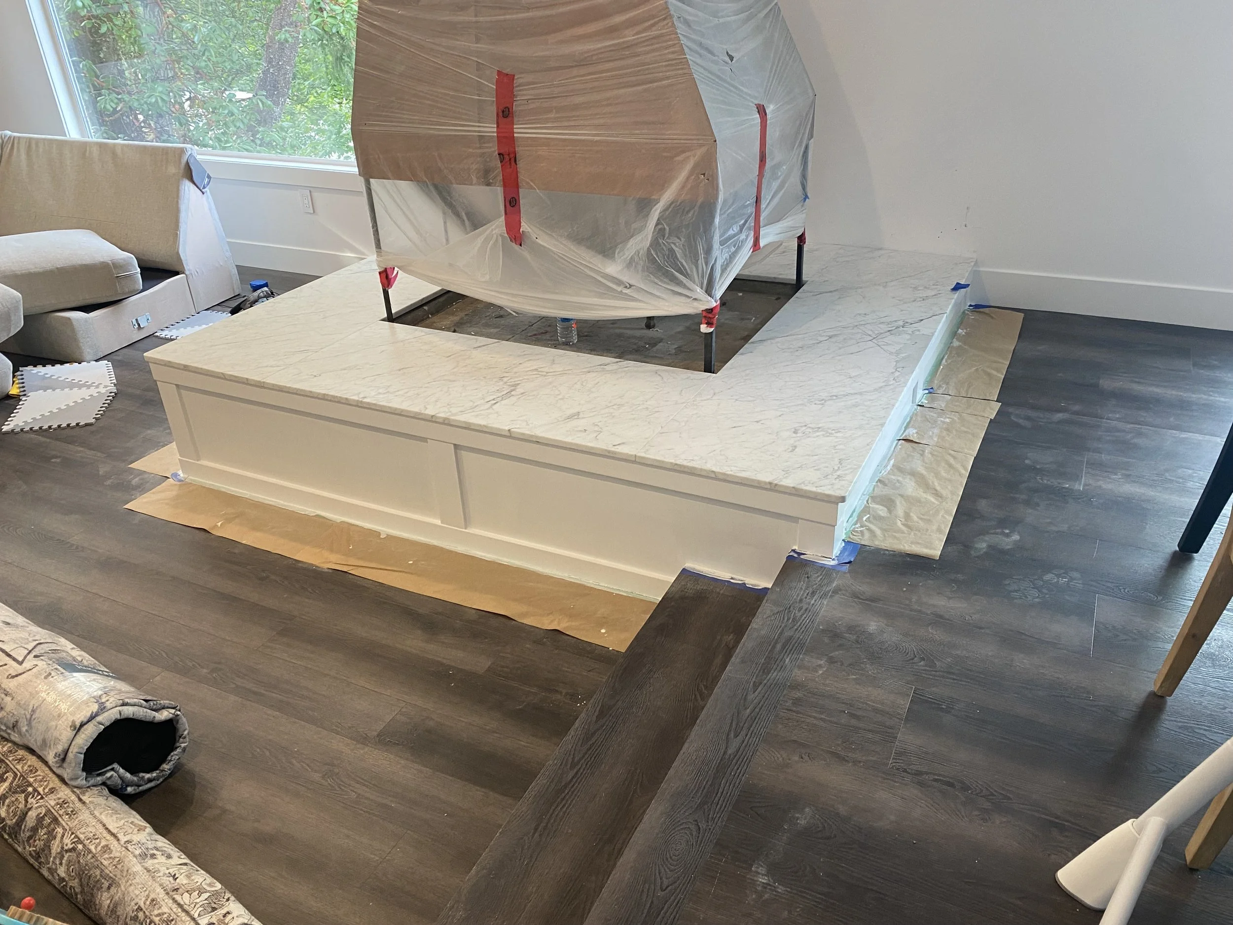 Room undergoing renovation with a large marble countertop, plastic sheeting, and tools scattered around.