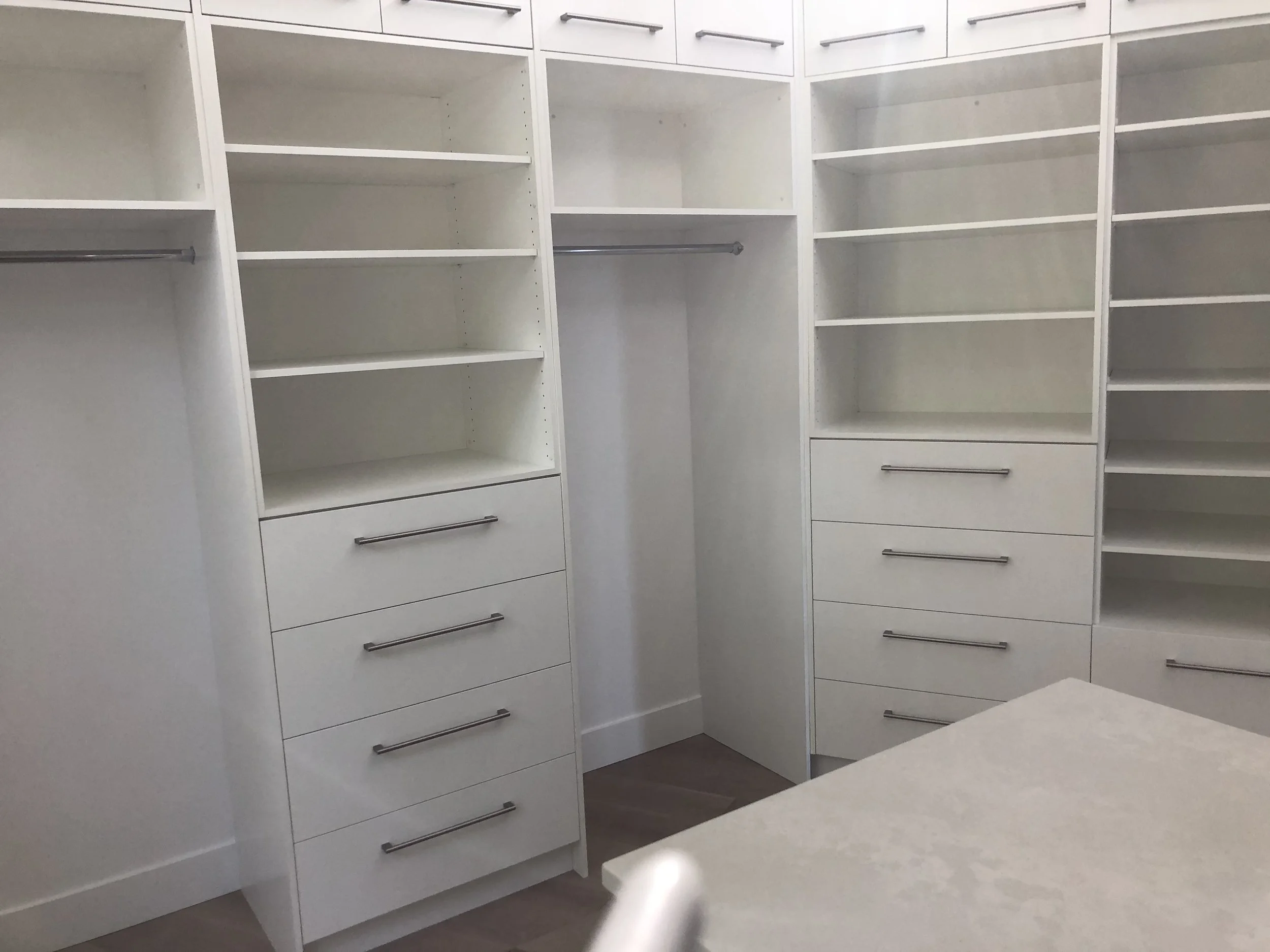 Empty white walk-in closet with multiple shelves, drawers, and hanging rods.