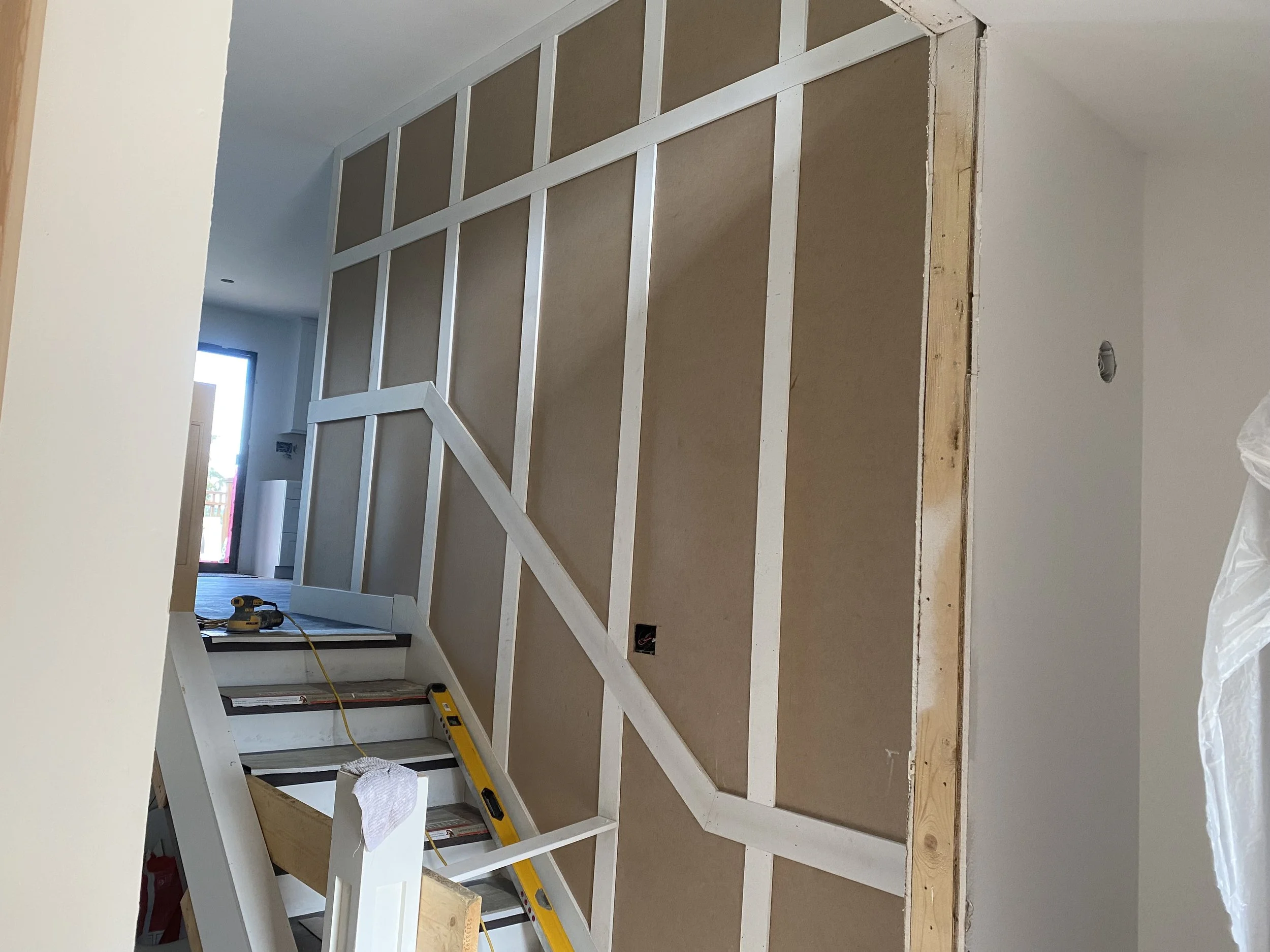 Interior of a room under construction with a wooden frame for a wall or door and construction tools, including a level and drill, placed on the floor.