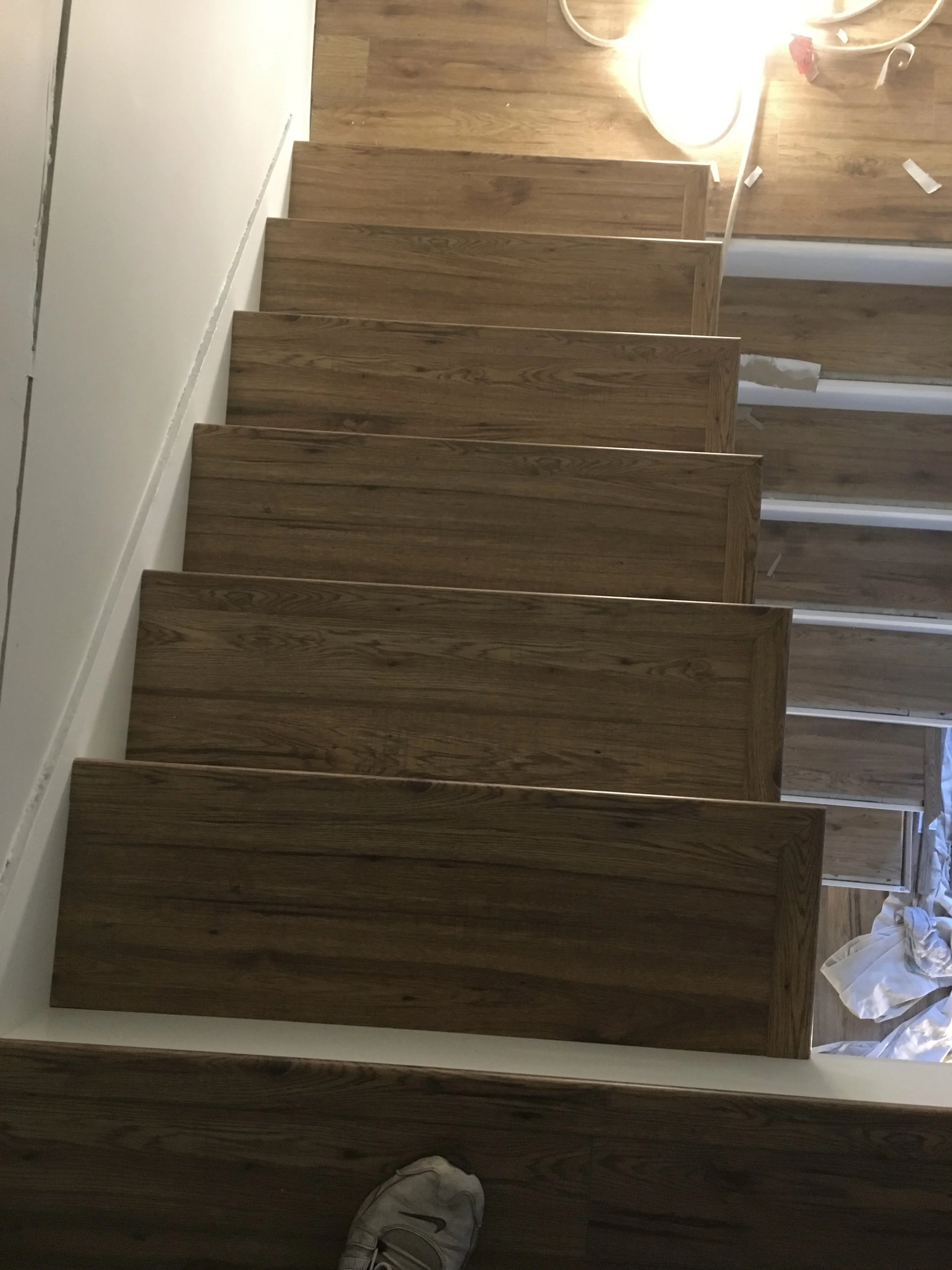 Stacked wooden kitchen backsplash or wall panels leaning against a white wall on a hardwood floor, with some debris and a shoe visible at the bottom right corner.