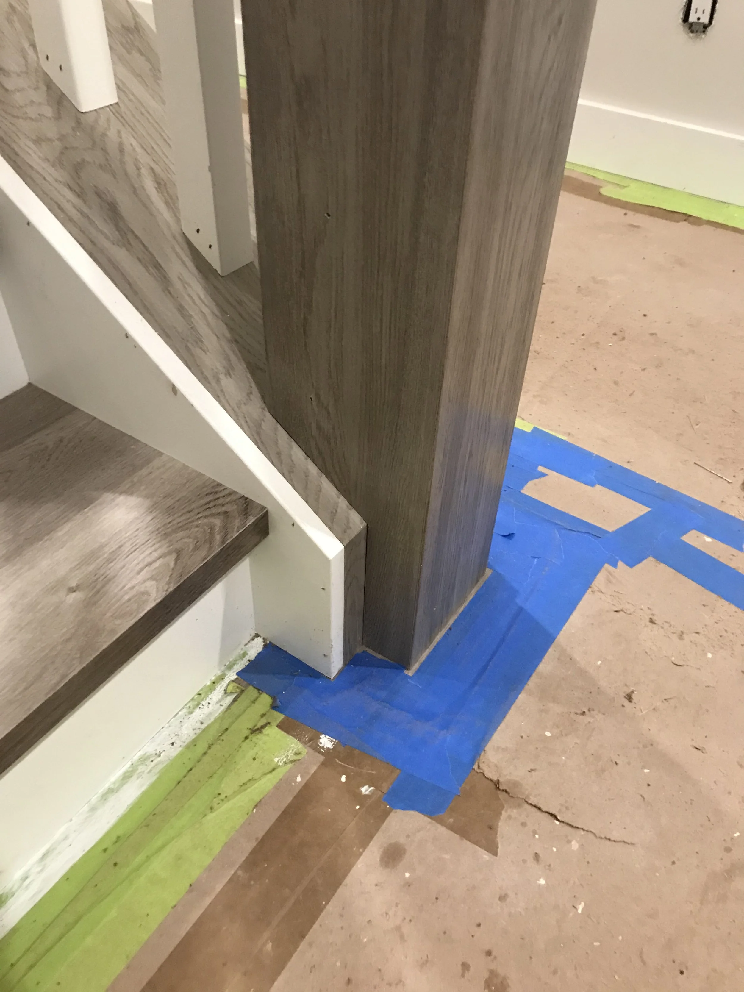 Partially constructed staircase with wooden steps, surrounding walls with visible drywall, and painter's tape on the floor, indicating ongoing renovation.