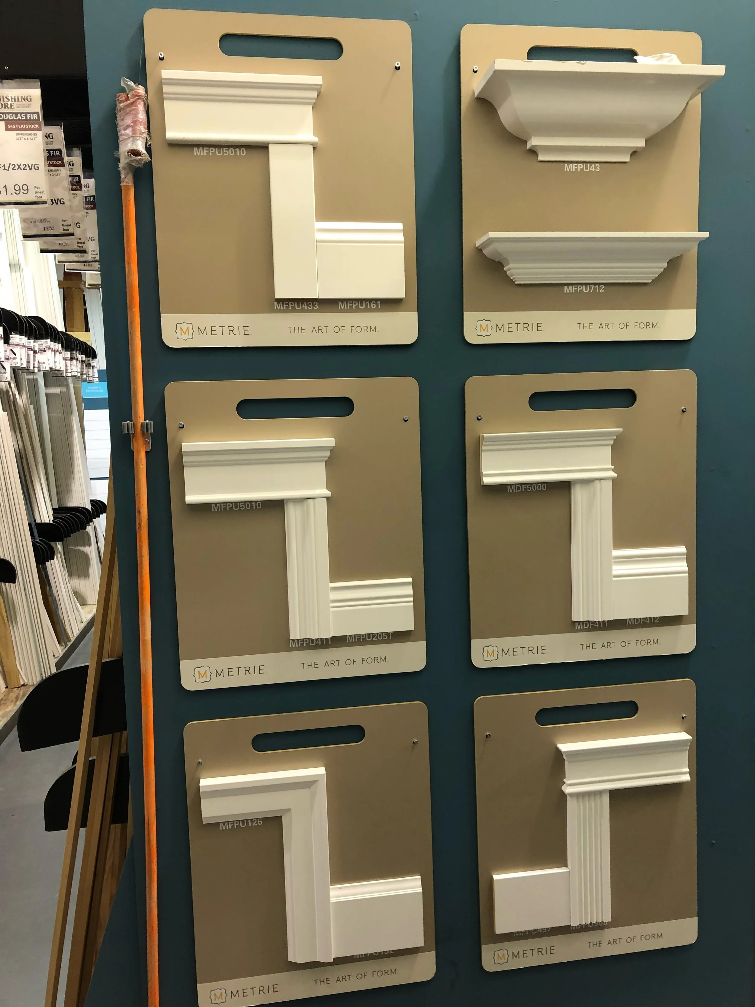 Display of various decorative architectural moldings and crown molding samples arranged on beige display boards in a hardware store.