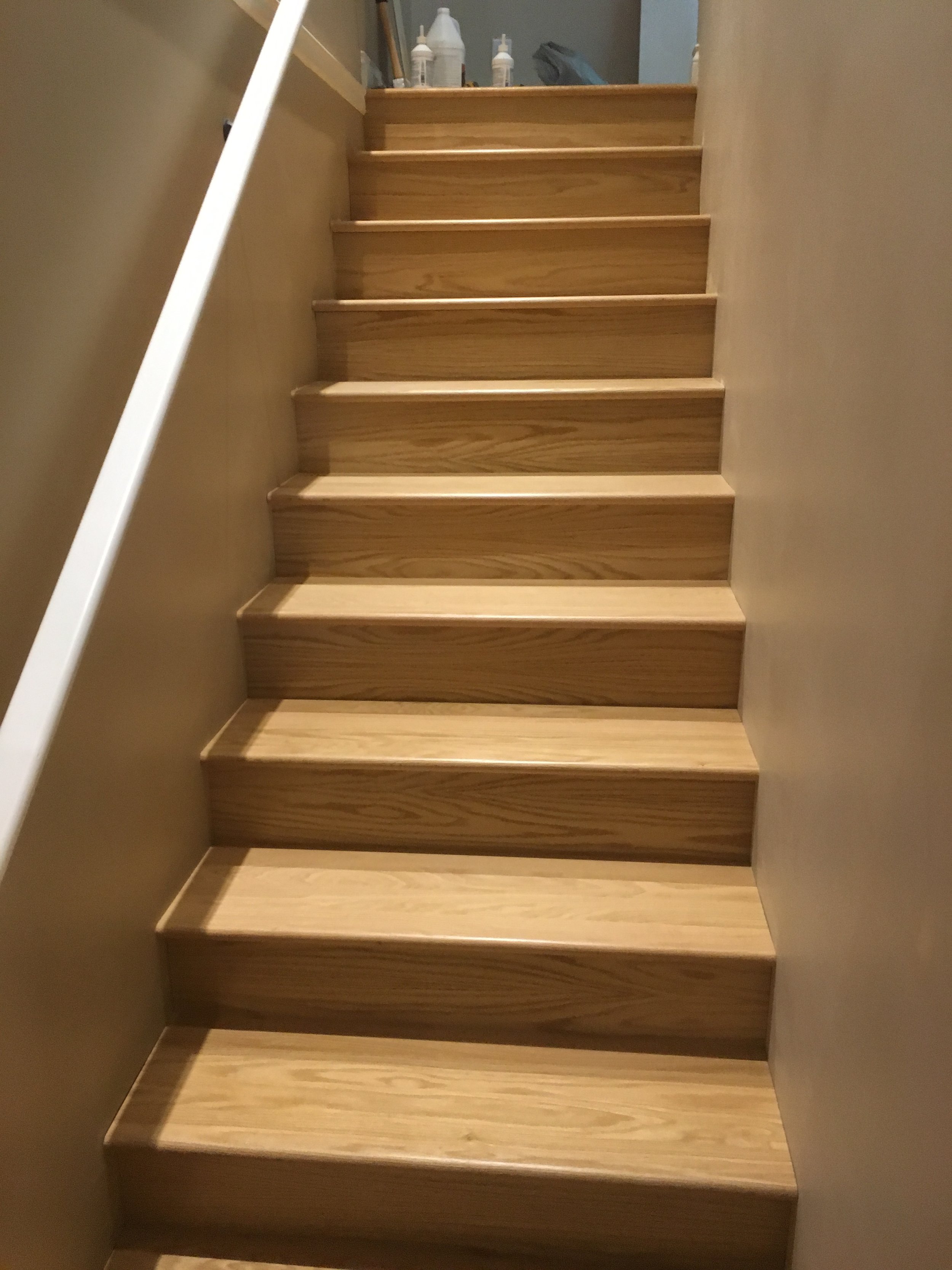 Wooden staircase with seven steps, walls painted light beige on either side, and some bottles and items visible at the top of the stairs.