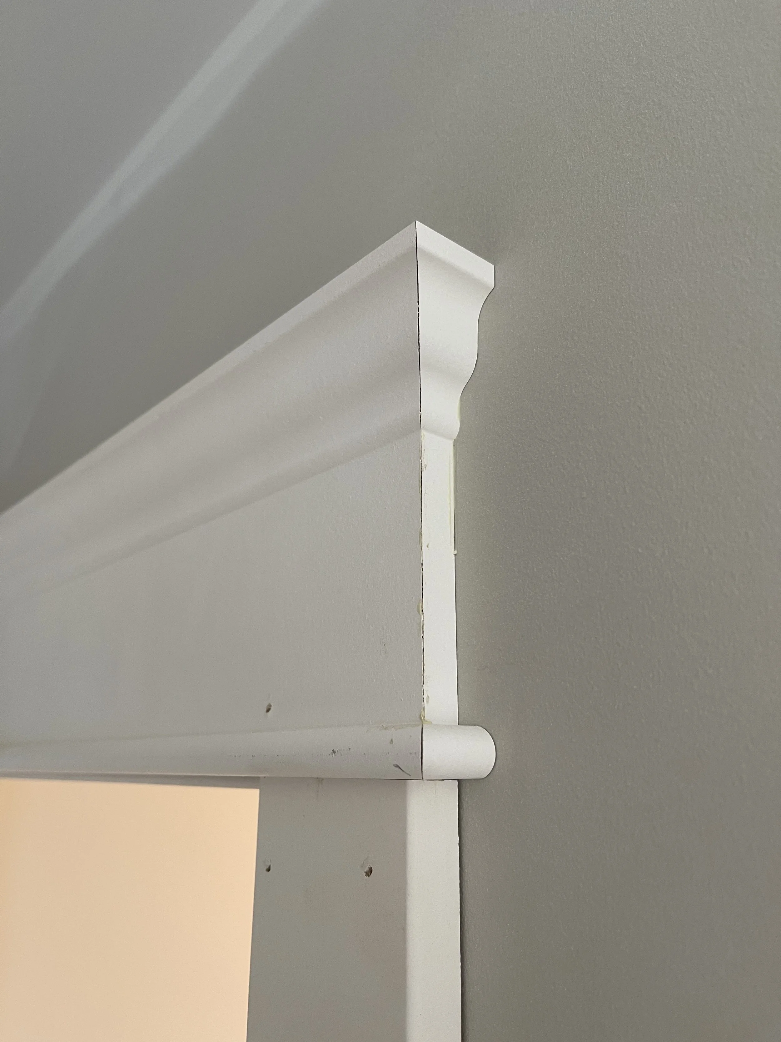 Close-up of a white window blind hanging from a ceiling or window frame, with a textured gray wall in the background.