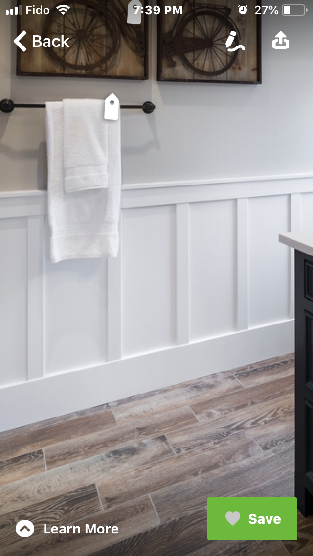 White towel hanging on a black towel rack against a white wall with wood paneling, and framed decorative wheels above.