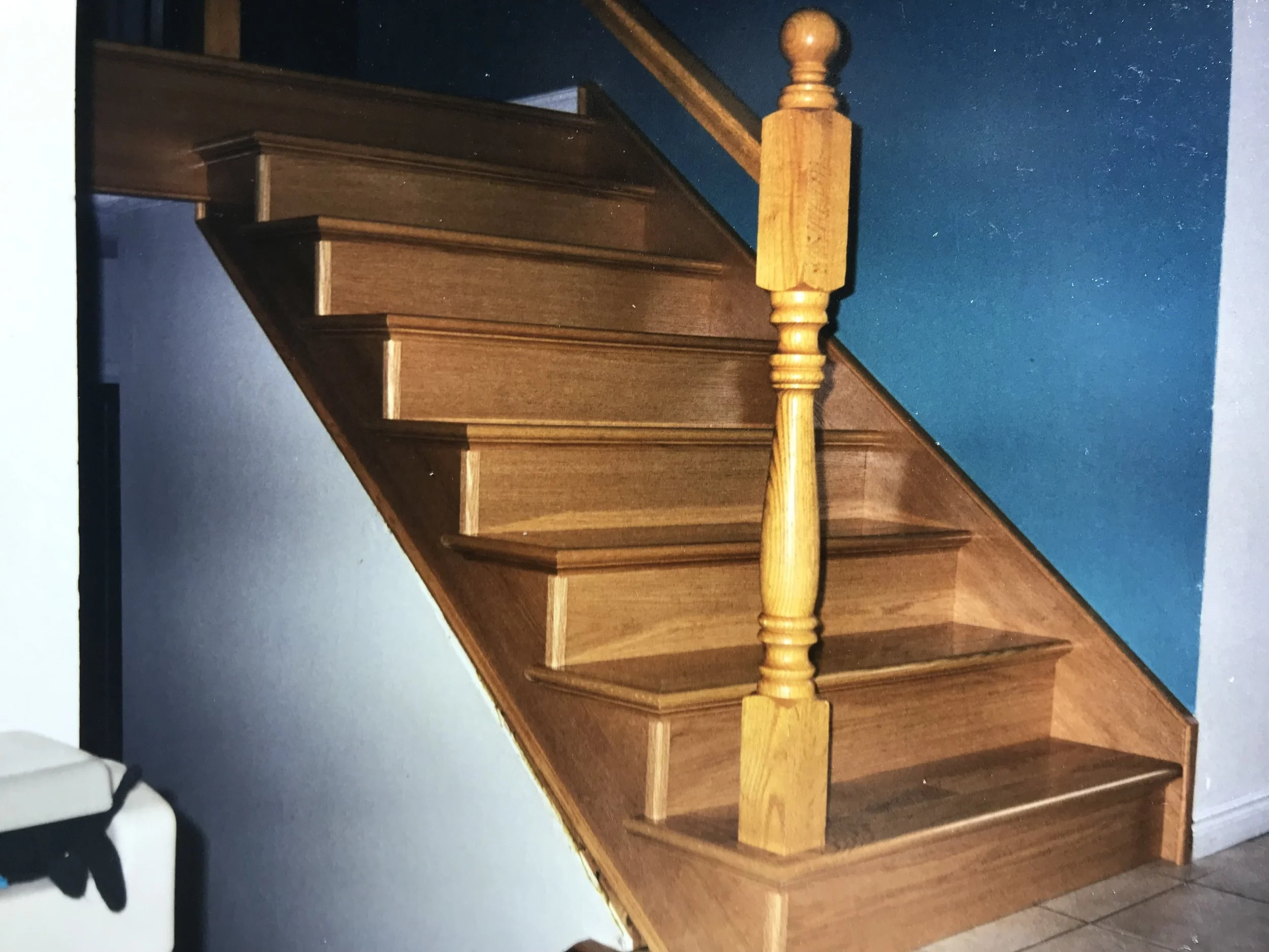 Wooden staircase with newel post and blue walls.