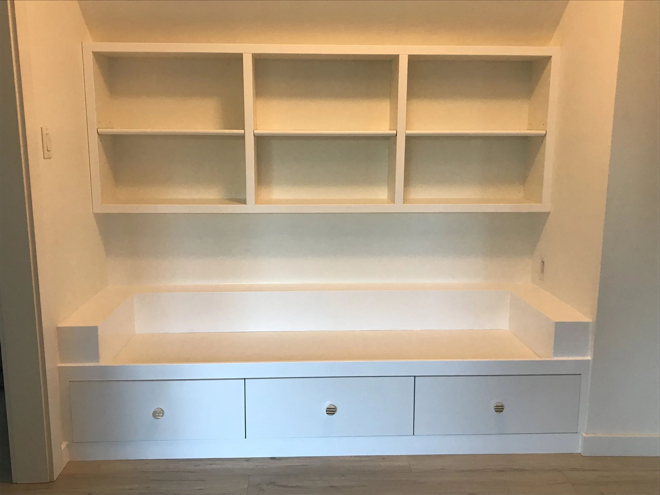 Empty built-in shelves and cabinet in a room with beige walls and wood flooring.