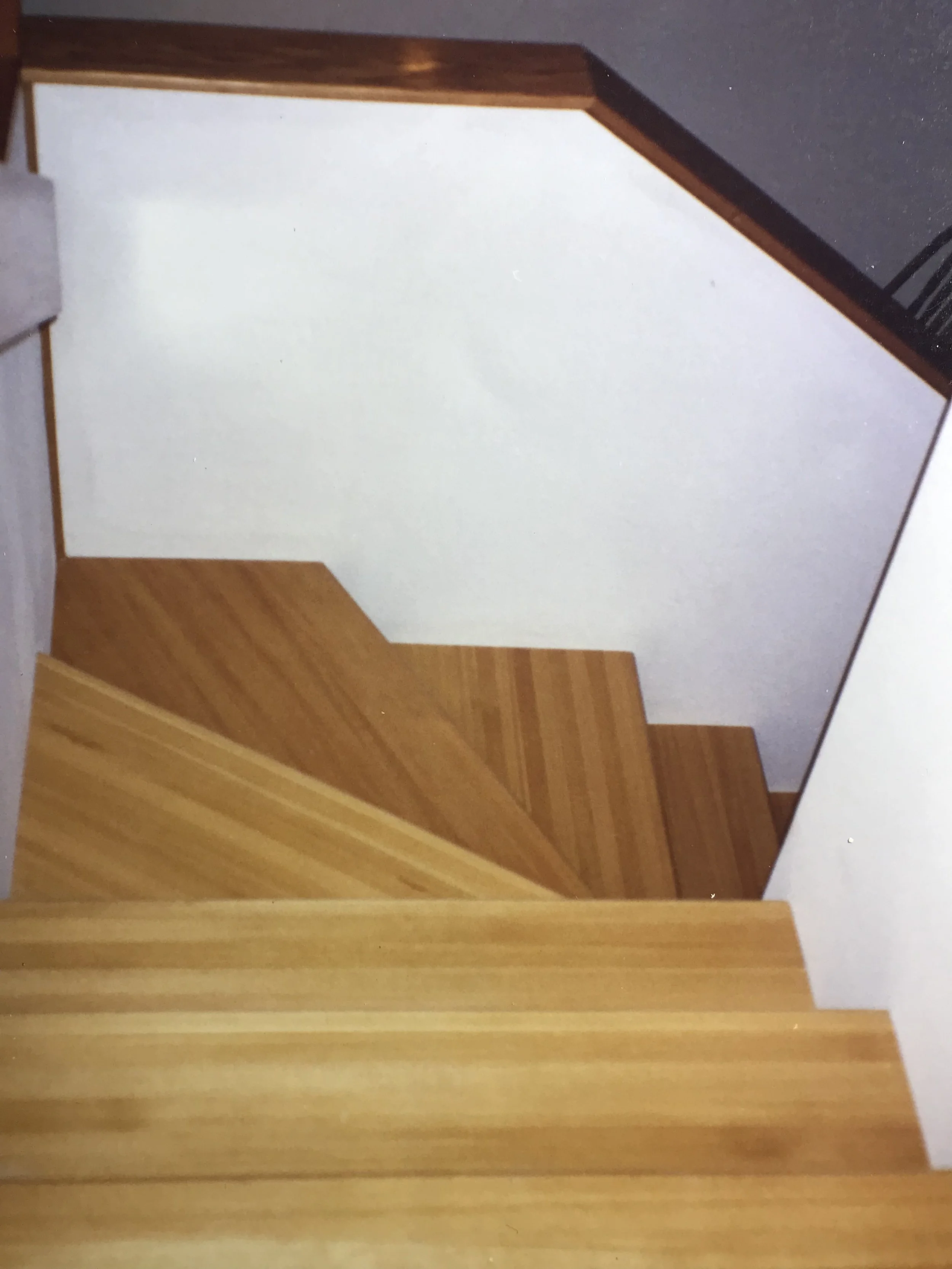 Photo of a wooden staircase with a white wall and a window