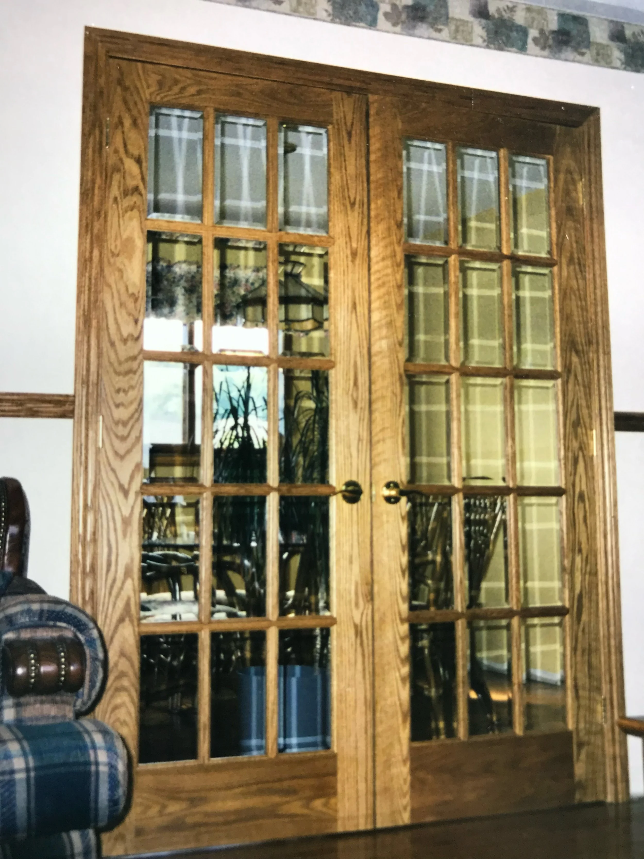 A wooden glass-paned door with curtains inside a room, reflecting an interior view with chairs and a table.