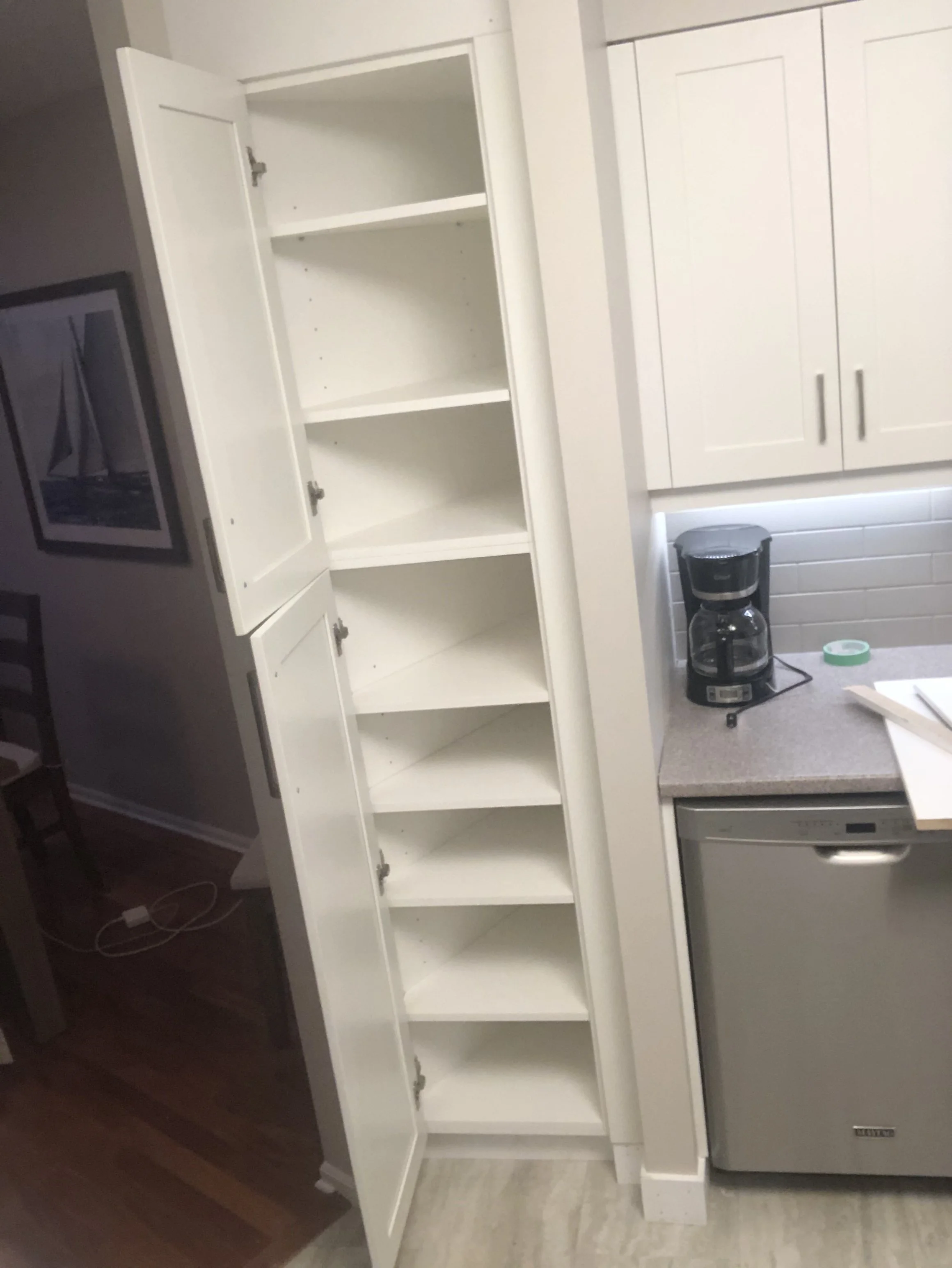 Empty white kitchen cabinet with open doors next to a coffee maker on the counter and a small dishwasher underneath.