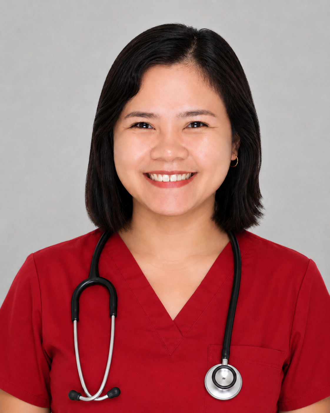 A smiling woman wearing red medical scrubs with a stethoscope around her neck, standing against a plain gray background.