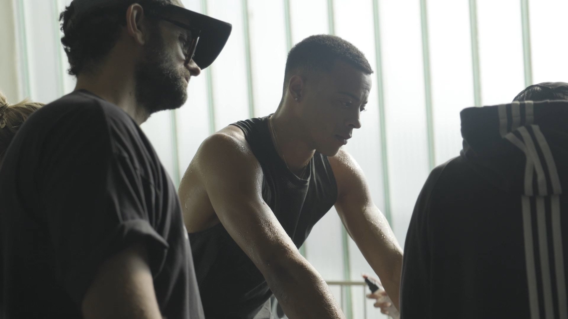Two men in athletic attire sitting near a window, possibly during a workout or sports activity, with one man sweaty and focused.