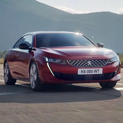 Red Peugeot sedan driving on a mountain road.