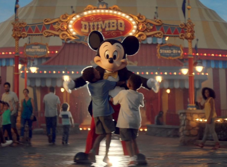 People, including children, dancing with Mickey Mouse costume character at Dumbo amusement park ride exit.
