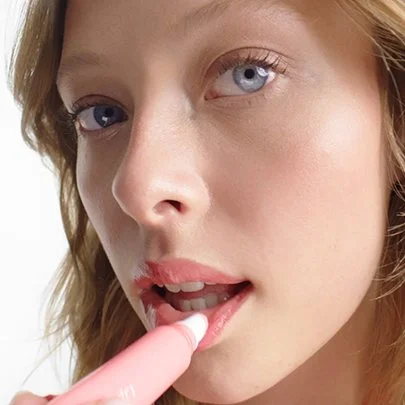 Close-up of a woman with blonde hair and blue eyes, touching her lips with a finger.