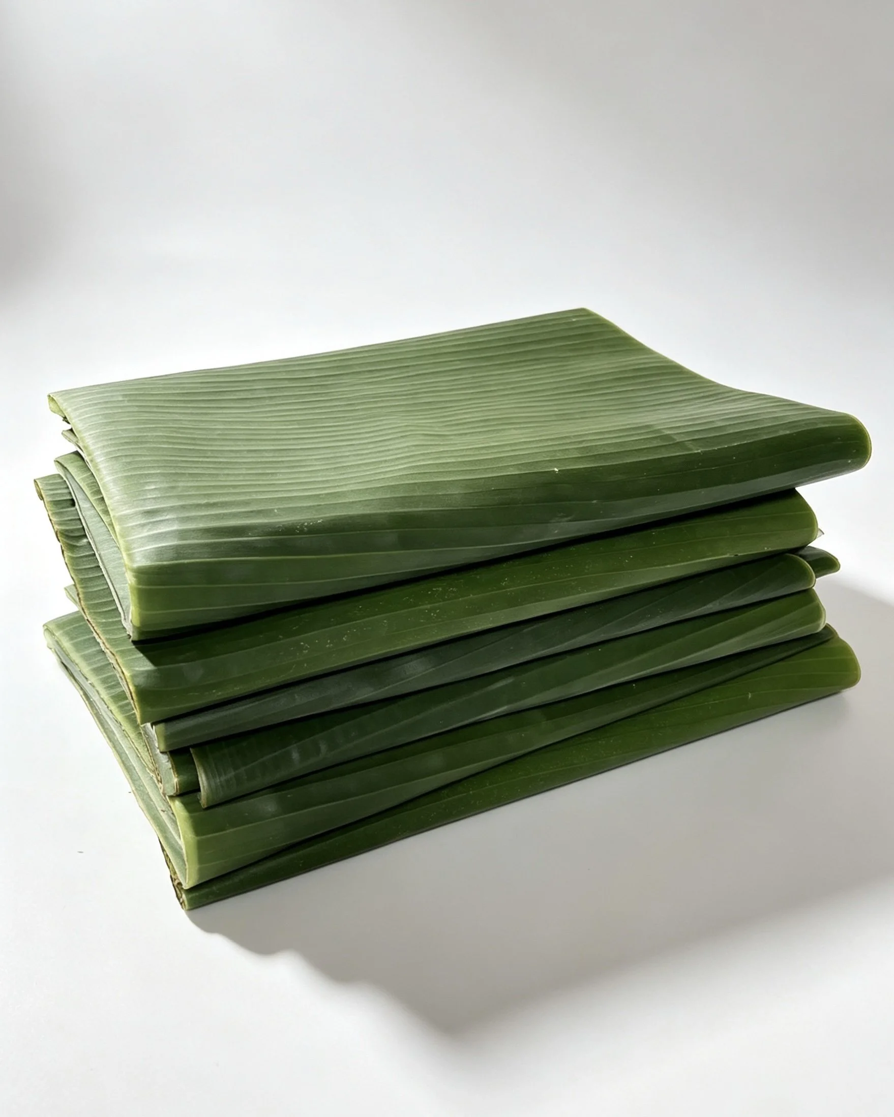 Stack of green banana leaves on a white surface.