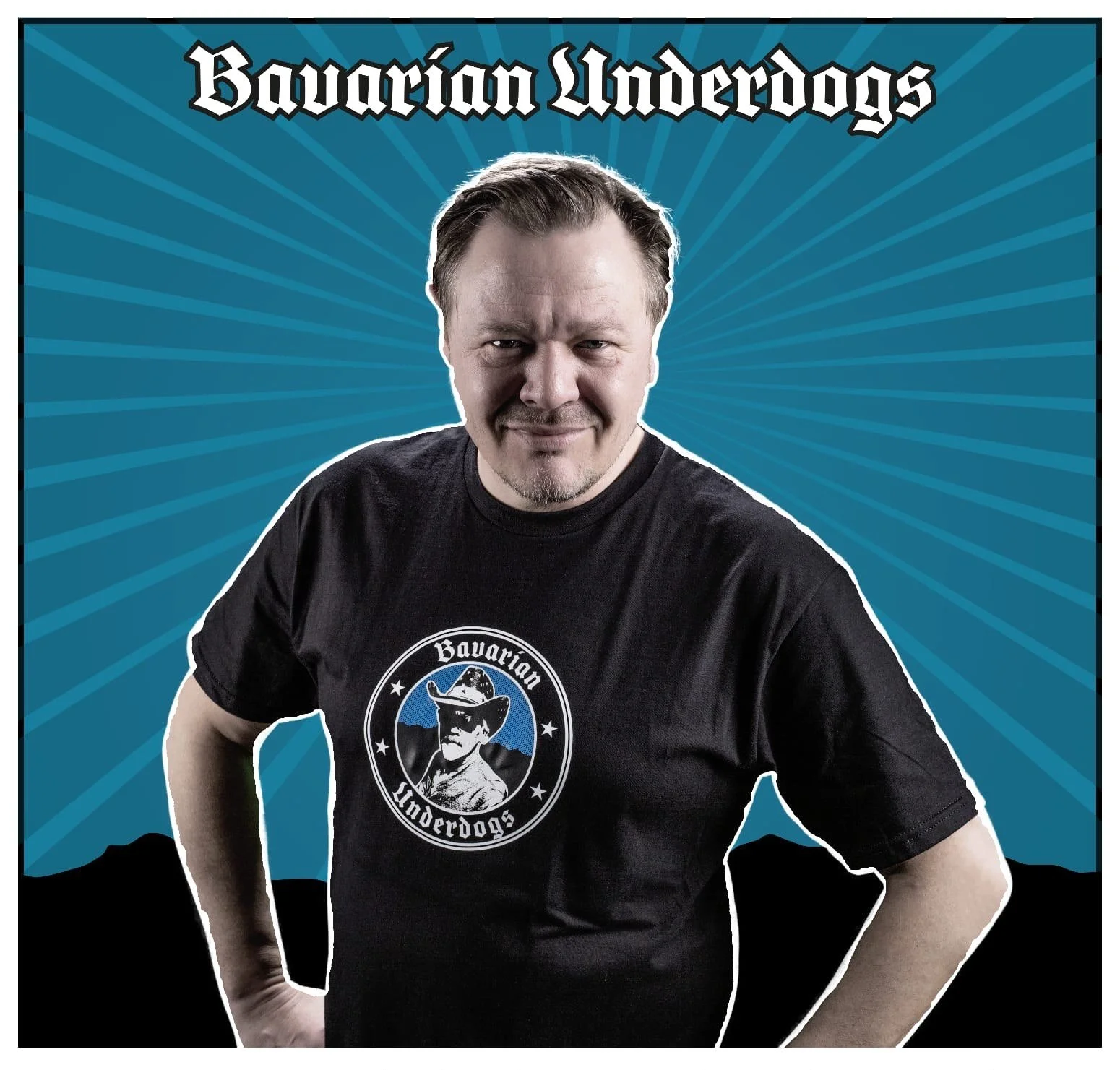 Elmar Voltz trägt ein schwarzes T-Shirt mit dem Logo der Bavarian Underdogs, ein Bier mit Hut. Im Hintergrund blauer Strahlenhintergrund mit dem Text "Bavarian Underdogs" oben.