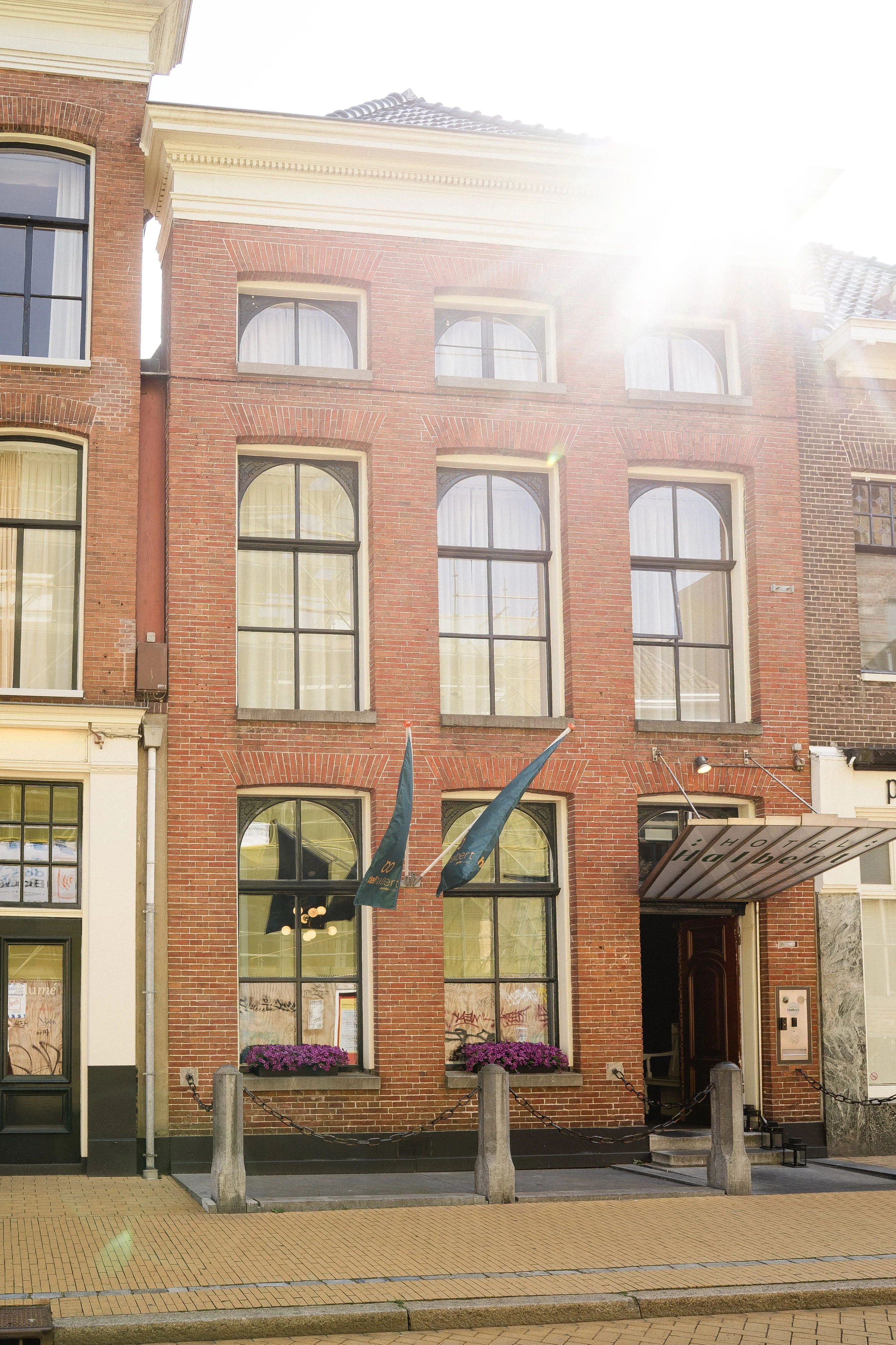 Brick building with large arched windows, purple flowers in window boxes, and an awning that reads 'Hotel Hohenzollern'.