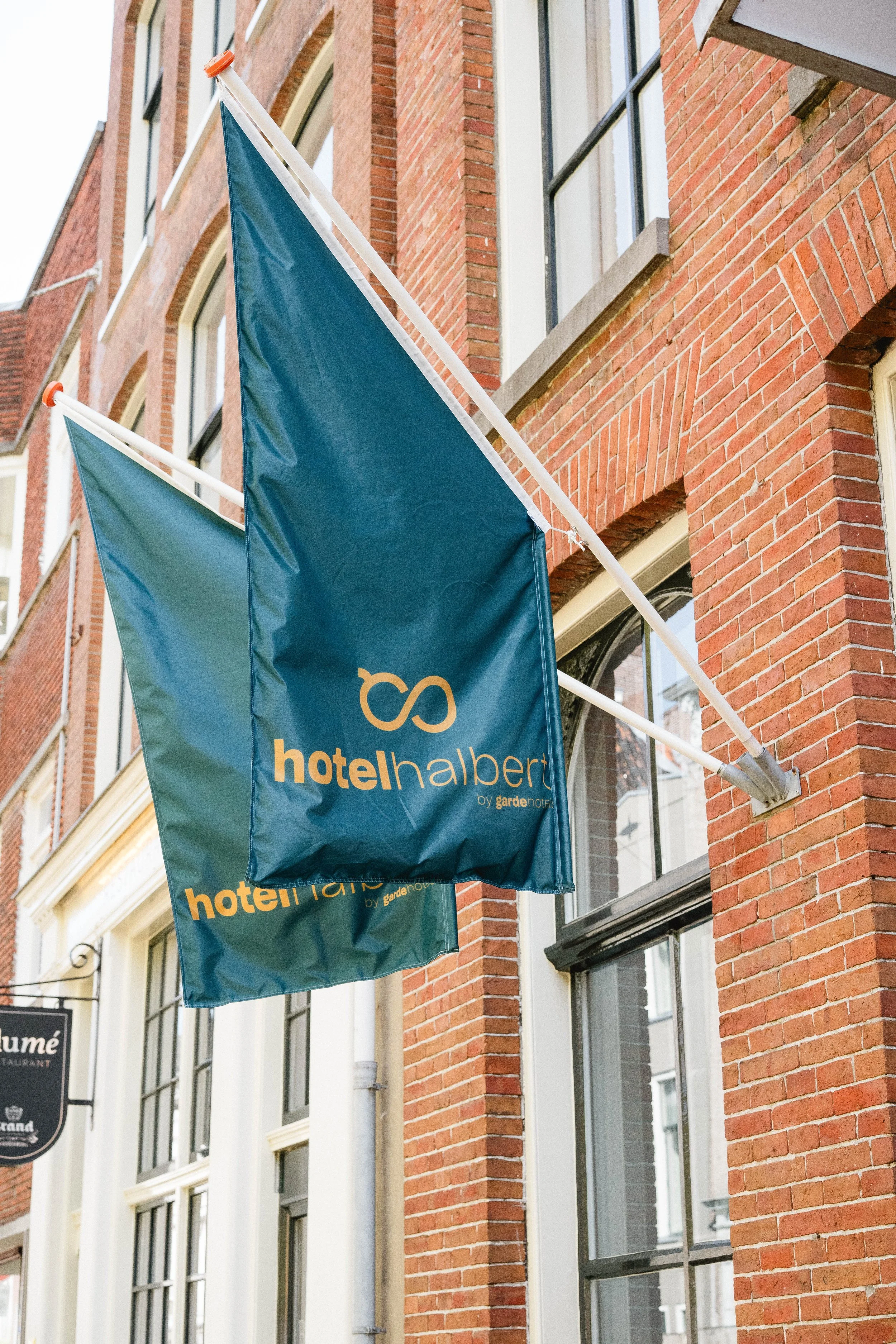 Two blue flags with yellow text hanging outside a red brick building.