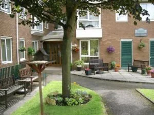 Apartment building courtyard with green grass, trees, benches, and potted plants.