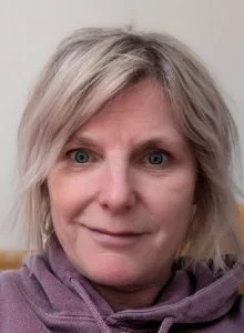 Close-up of a woman with short blonde hair wearing a purple scarf.