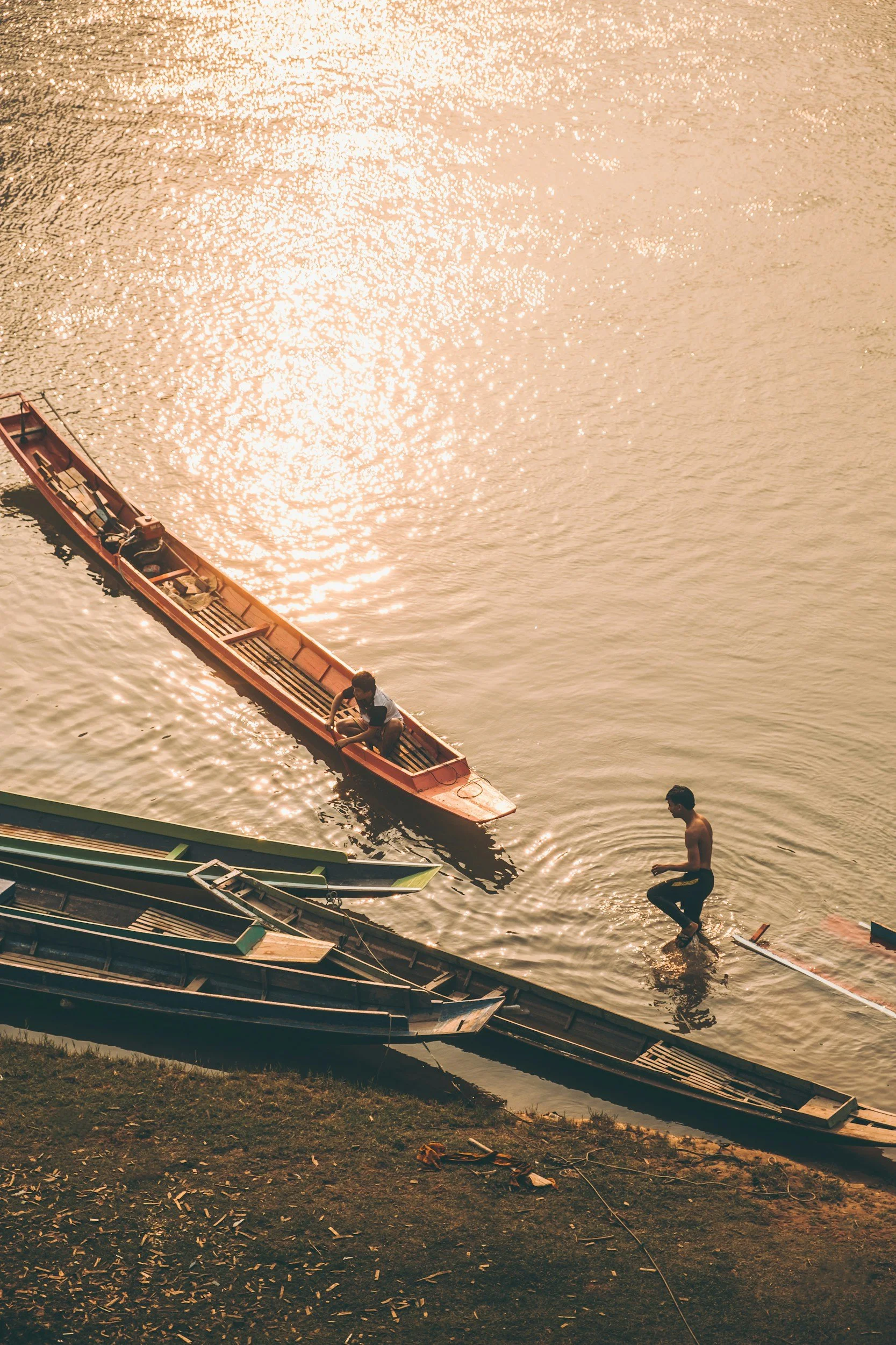 Des garçons jouent près d'un bateau à l'eau au Laos, certains étant dans l'eau tandis qu'un garçon est debout au bord.