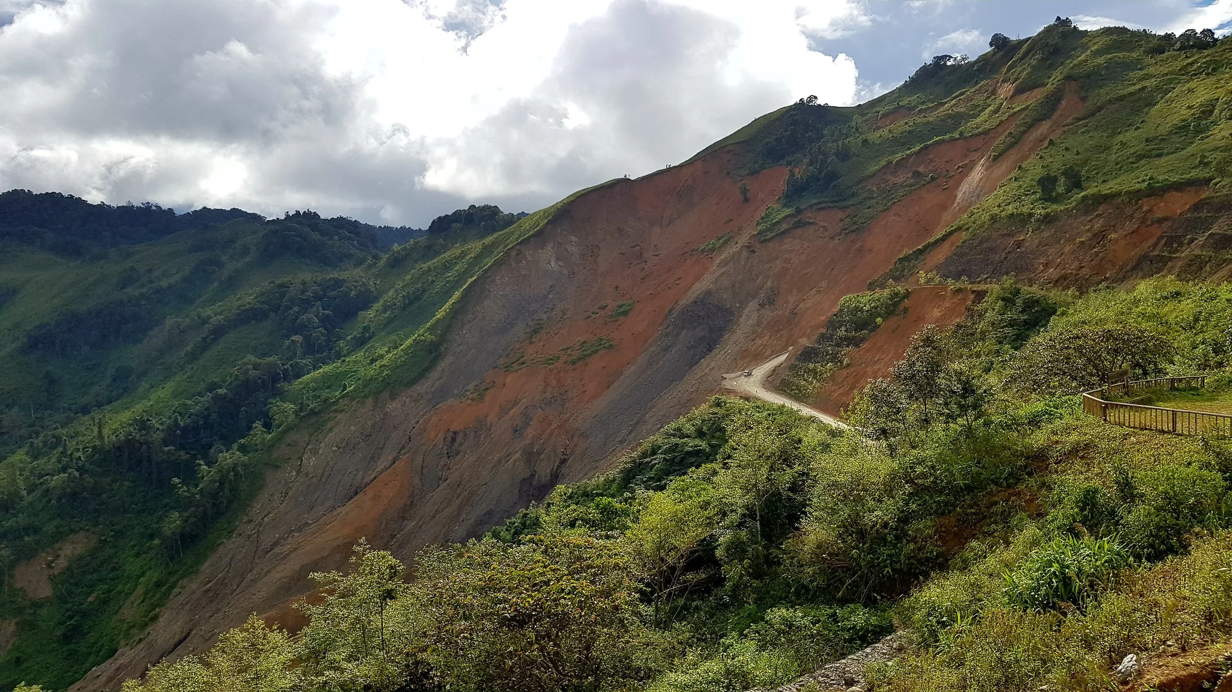 Montagnes verdoyantes avec une route sinueuse et un parc en bois dans une zone de débris de terres glitchées.