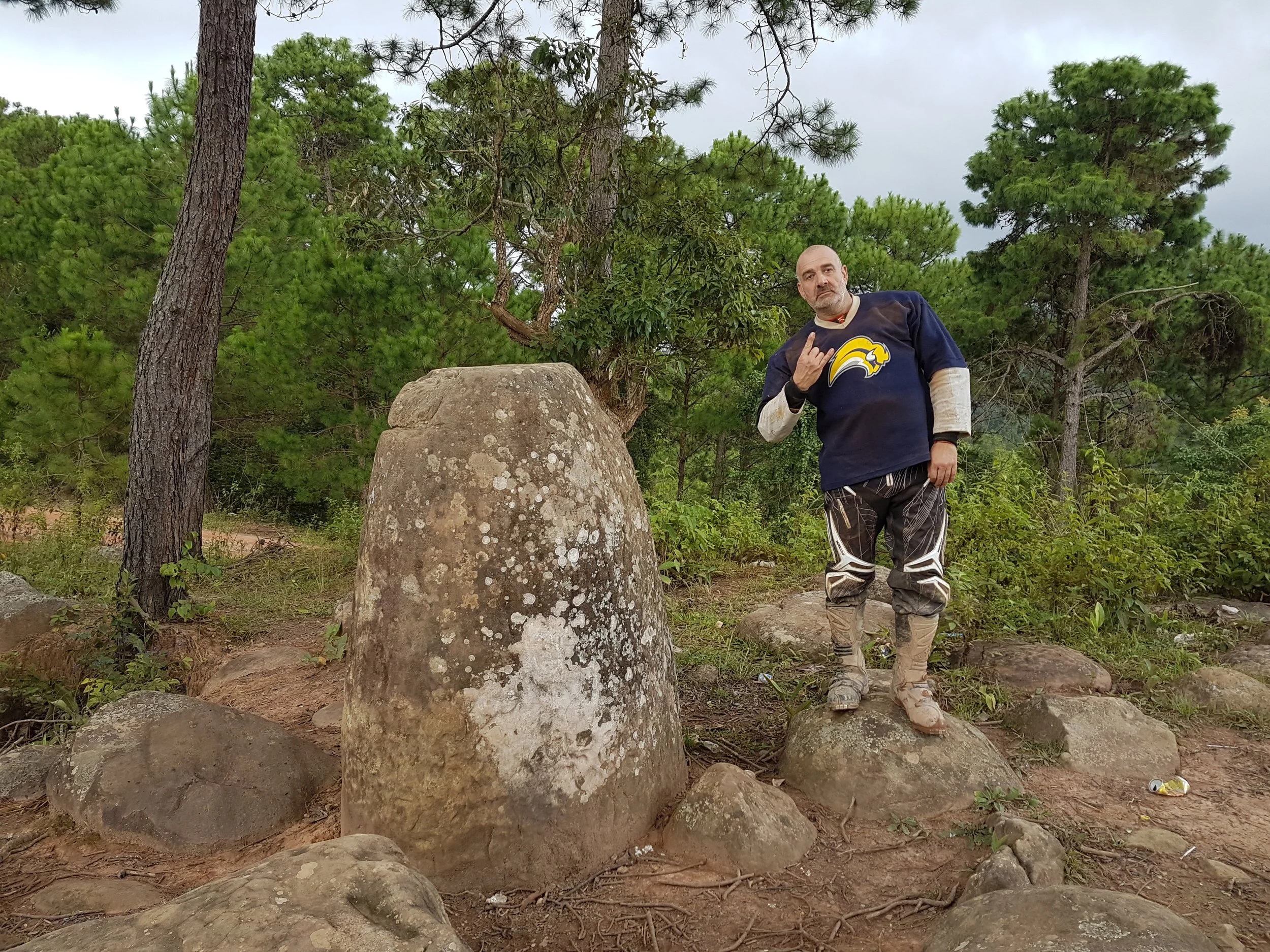 Un homme pose devant un arbre dans la nature, portant un maillot de hockey de style football américain, faisant un geste de la main.