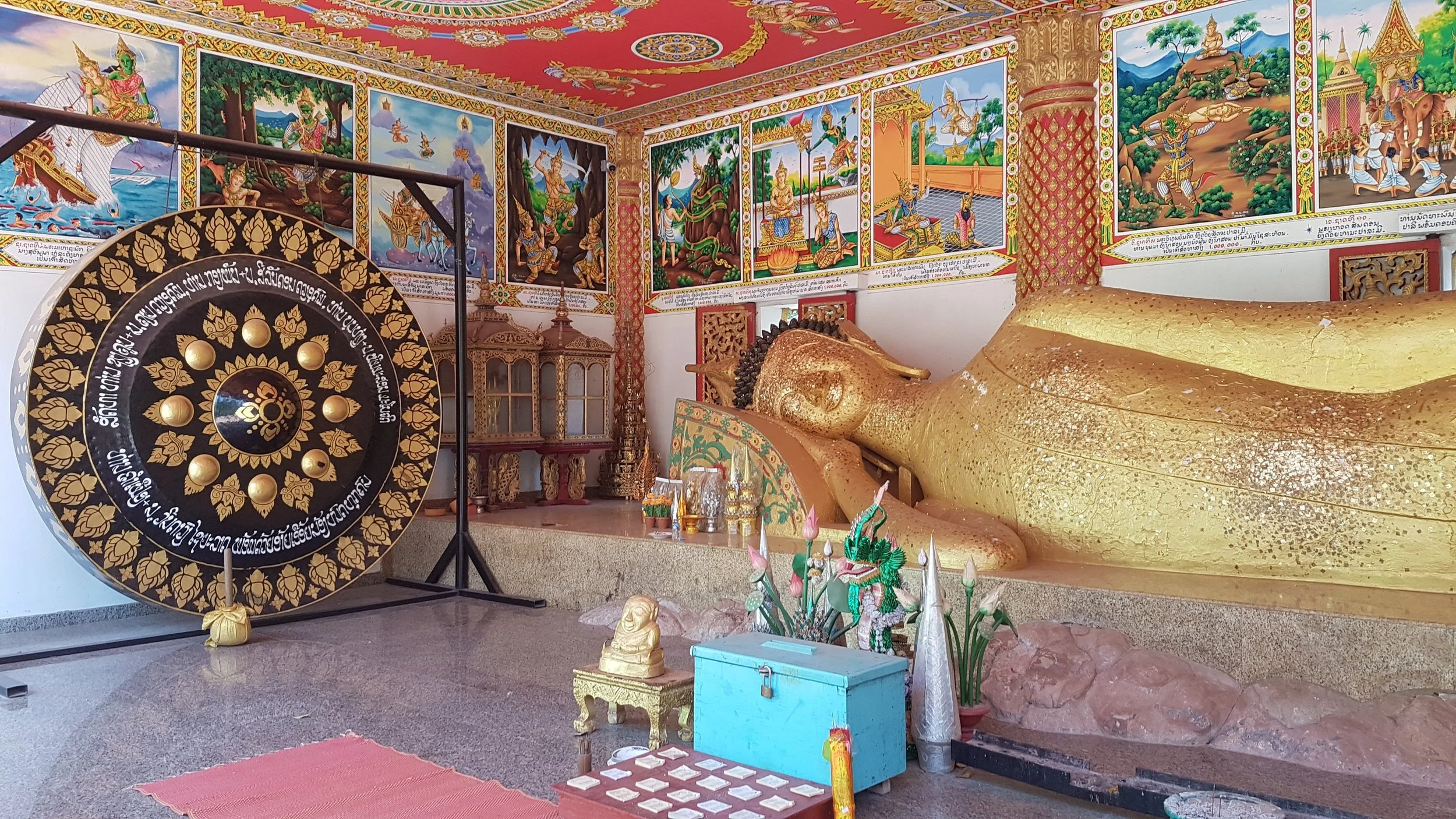 Une représentation d'une scène religieuse thaïlandaise avec un grand lit doré pour Buddha, des peintures murales colorées, un tambour traditionnel et des petits objets de culte.