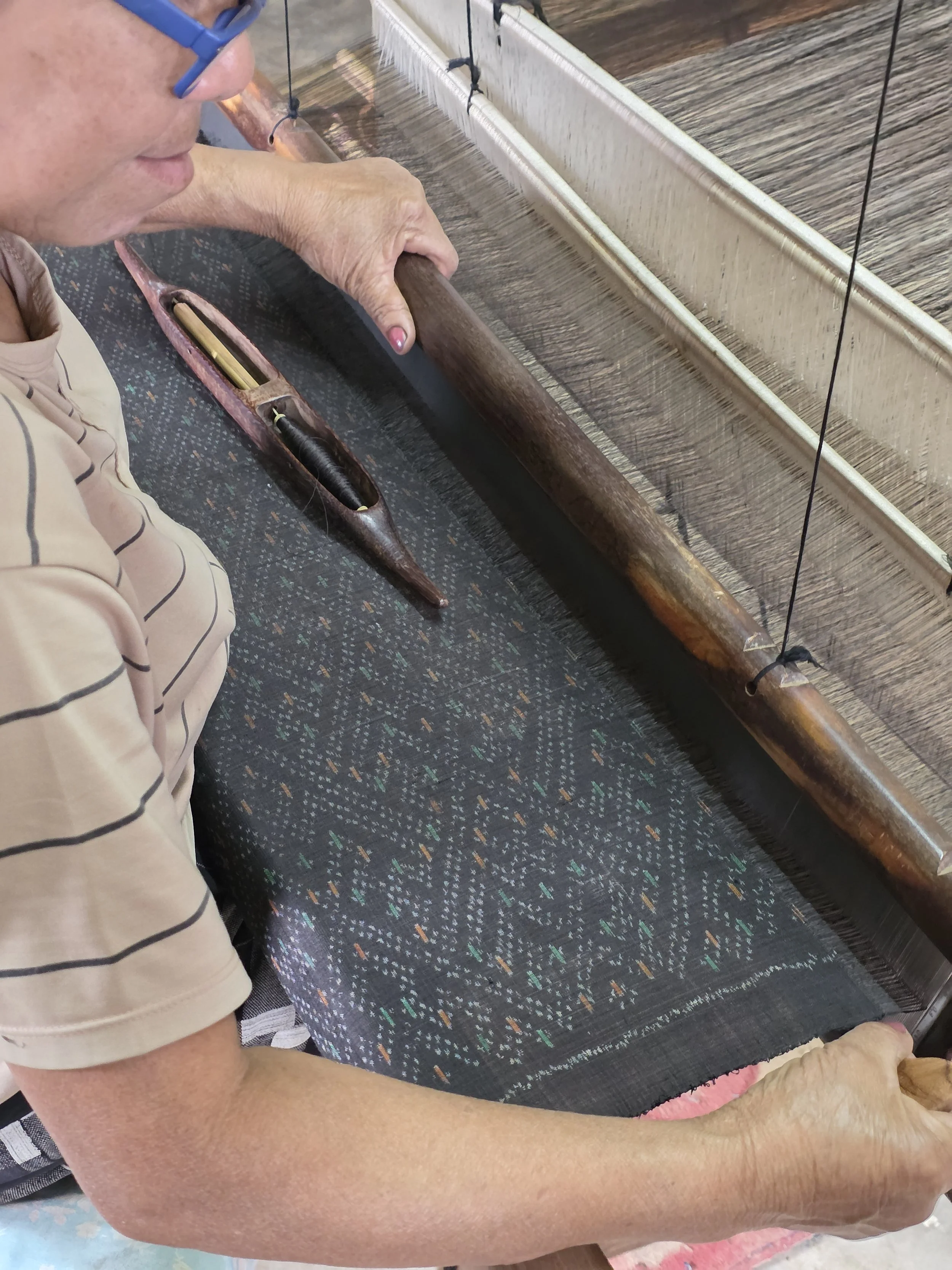 Une personne âgée travaillant sur un métier à tisser traditionnel en bois, en train de faire de la tapisserie ou du tissage.