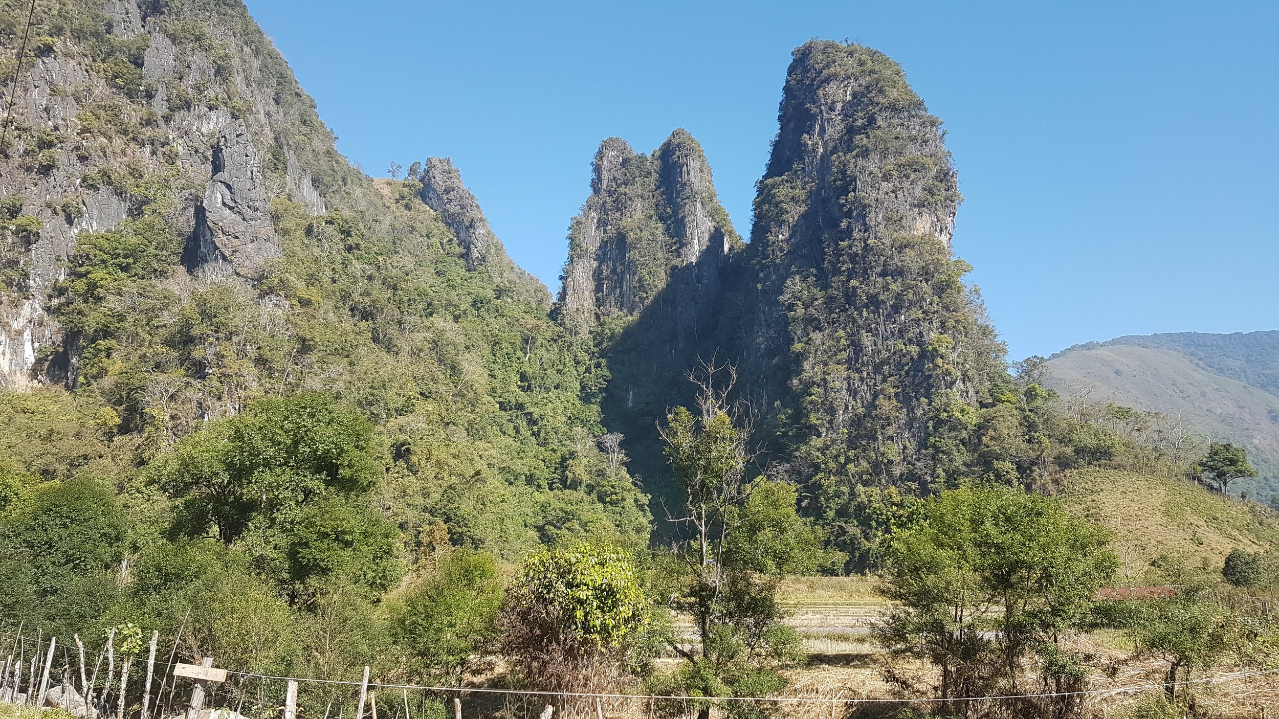 Montagnes rocheuses couvertes de verdure sous un ciel bleu clair.
