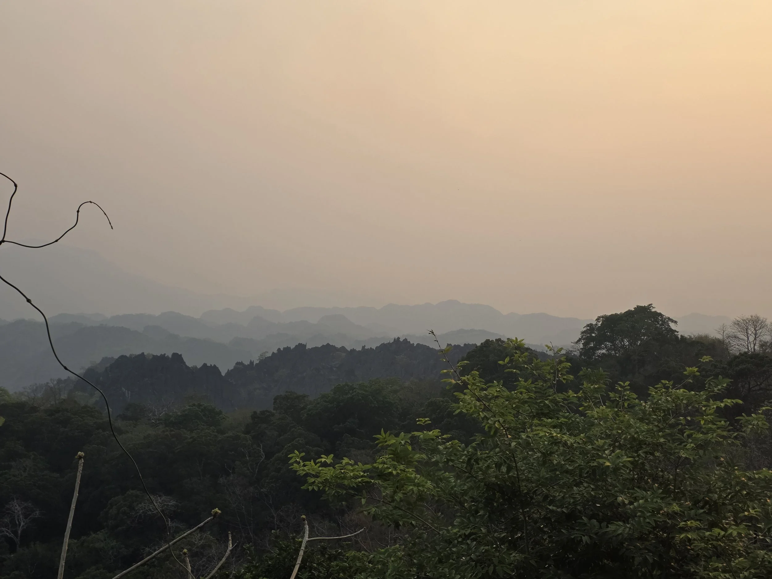 Vallée montagneuse couverte de forêt avec un ciel nuageux. Laos