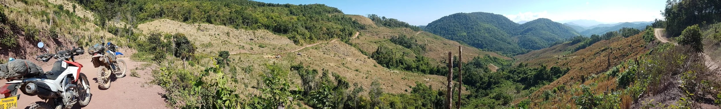Vue panoramique de montagnes verdoyantes avec une route de terre sinueuse et des motos garées sur le côté.