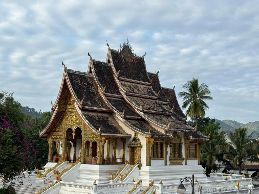 Un temple traditionnel thaïlandais avec un toît en pignon et des décorations dorées, entouré de palmiers et de végétation tropicale.